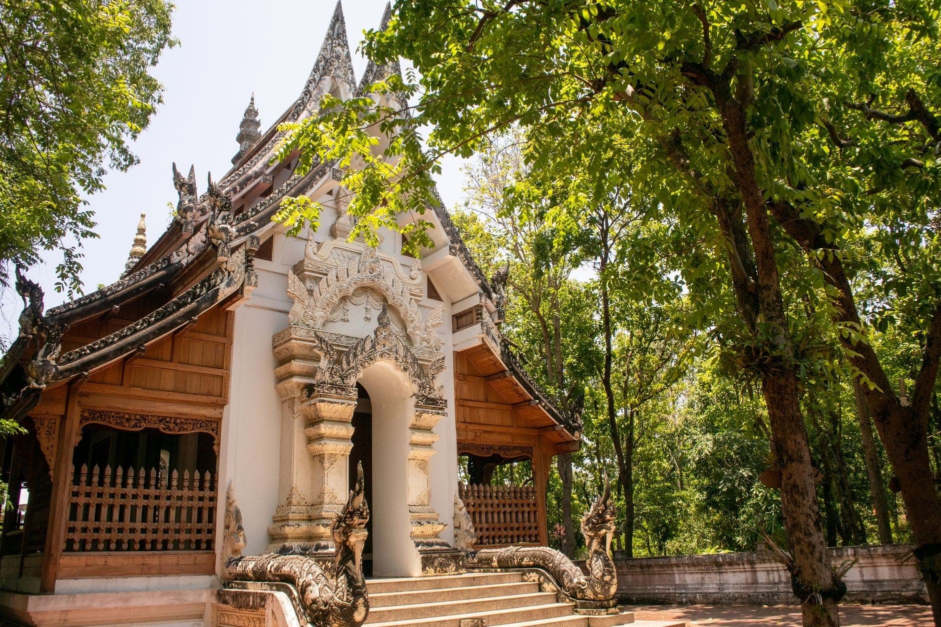 Edificio tempio tradizionale in stile Lanna con intricati intagli in legno e facciata bianca, circondato da lussureggianti alberi verdi a Chiang Mai.