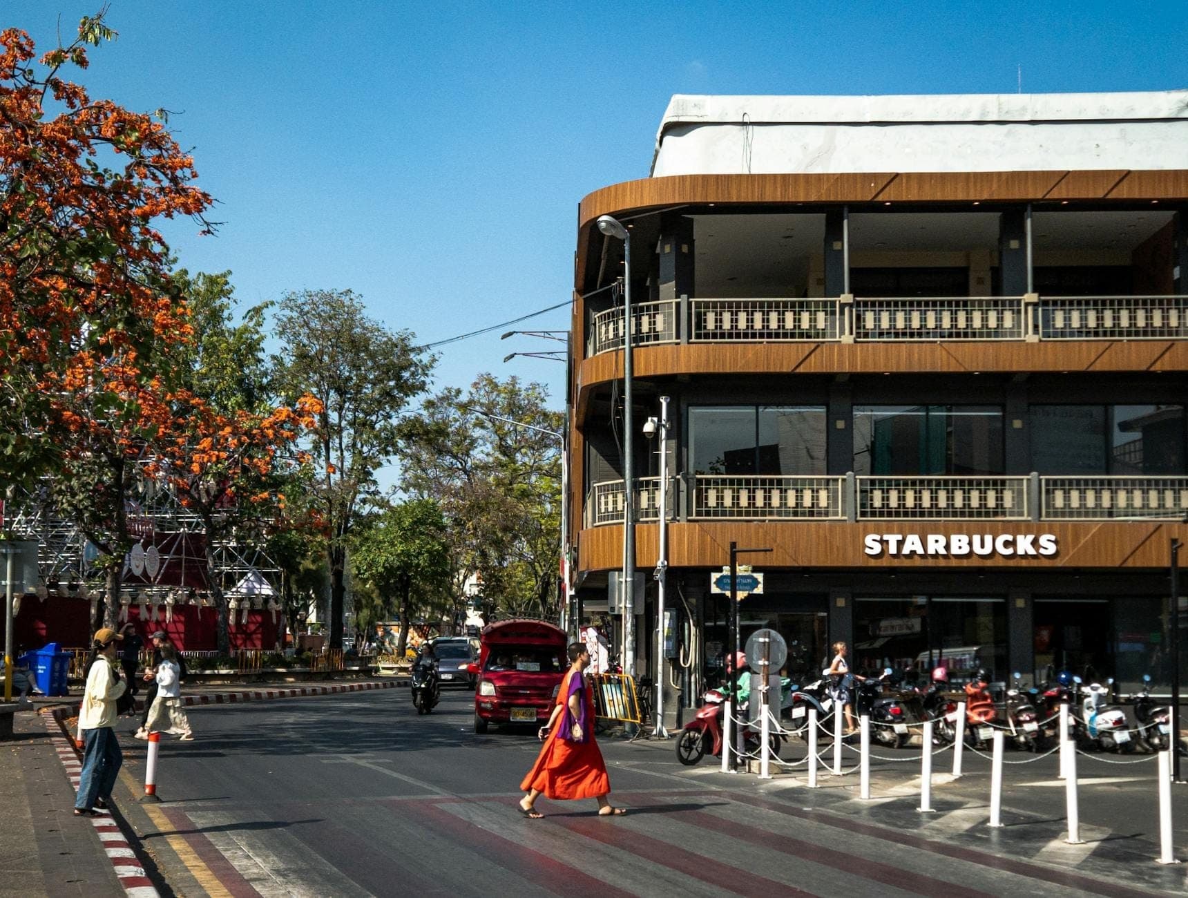 Chiang Mai'de Tha Phae Kapısı yakınında, kahverengi bir Starbucks binasının önünden geçen bir keşiş ve dışarıda park edilmiş motosikletlerle sokak sahnesi.