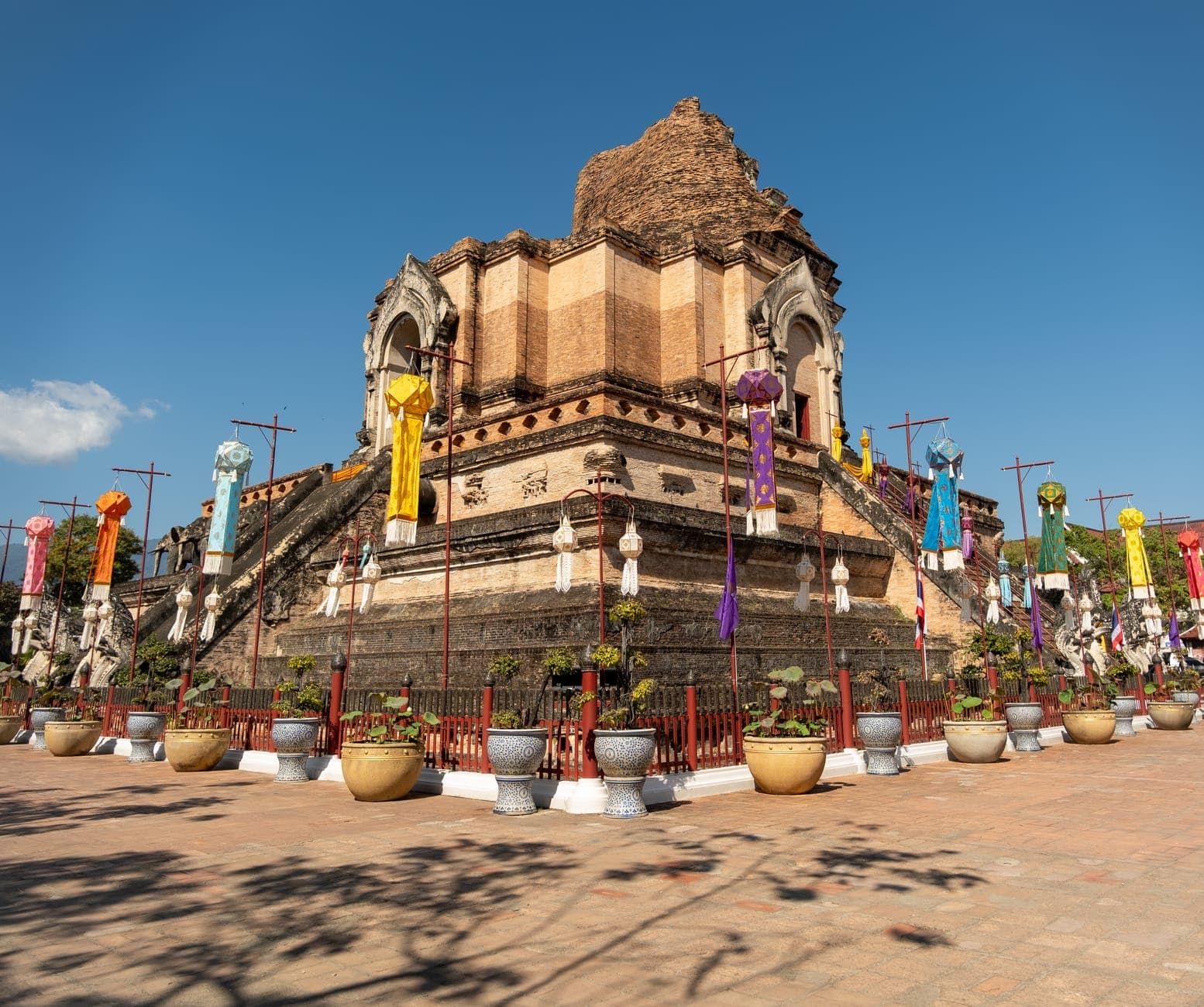 Weitwinkelansicht des alten Backsteinchedi von Wat Chedi Luang mit bunten Tempelfahnen und strahlend blauem Himmel – das Wahrzeichen der Chiang Mai Altstadt in leuchtendem Tageslicht.
