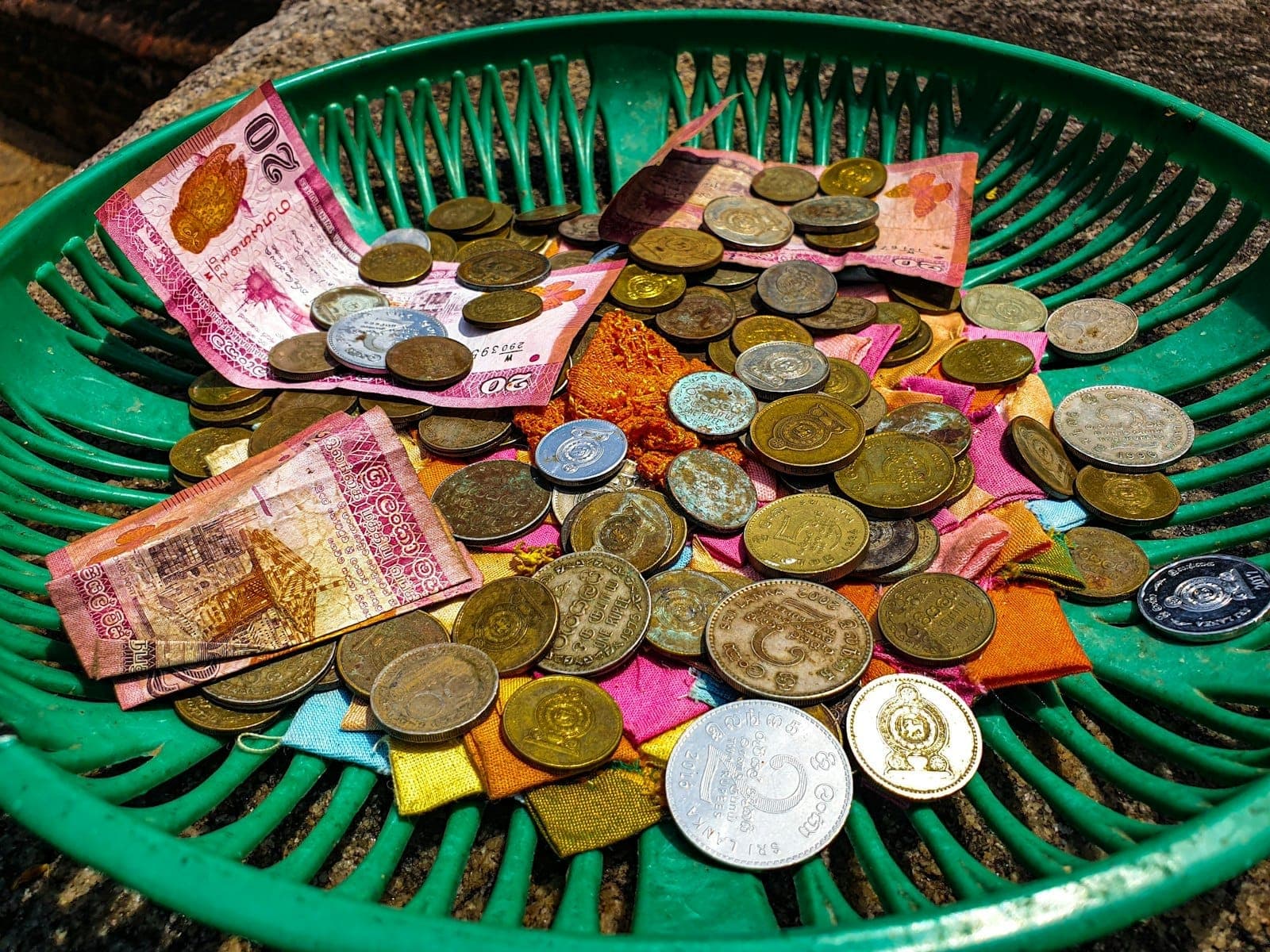 Nahaufnahme von thailändischen Baht-Münzen und -Banknoten in einem grünen Korb, mit Sonnenlicht, das die in Chiang Mai gebräuchliche Landeswährung hervorhebt.