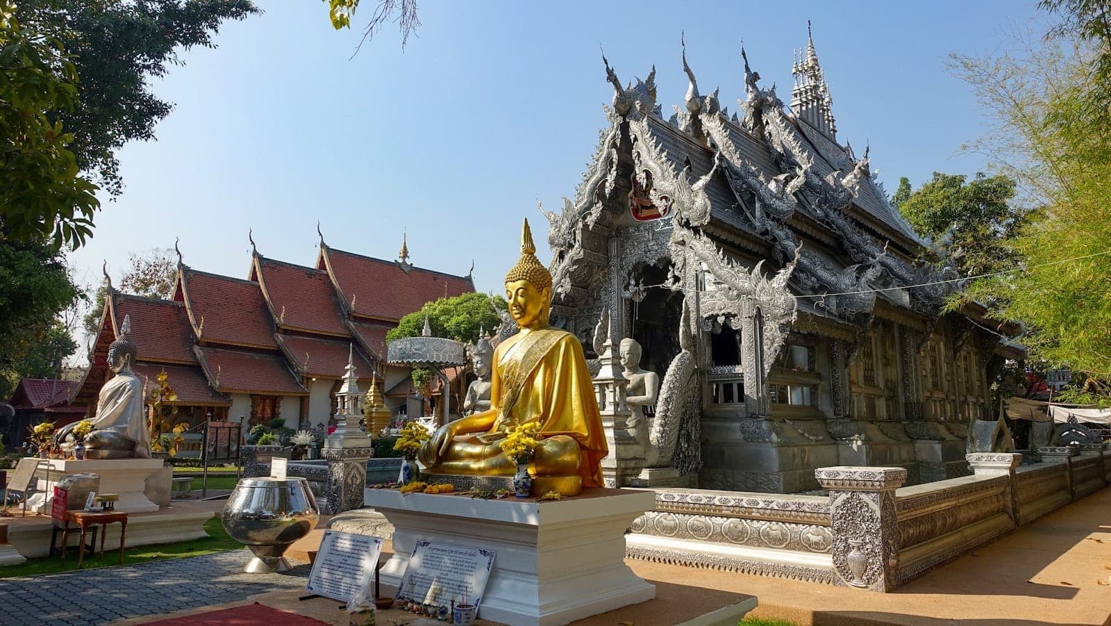 Złota statua Buddy i zdobna srebrna świątynia w Wat Sri Suphan w Chiang Mai w jasnym słońcu.