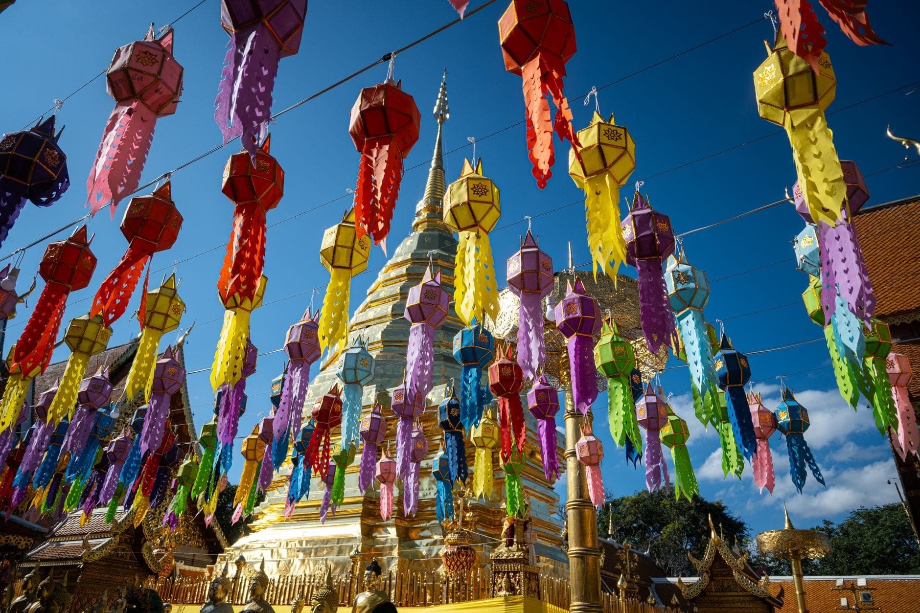 Bunte Papierlaternen vor einem goldenen Tempel in Chiang Mai mit strahlend blauem Himmel – festliche Stimmung pur in Thailand.