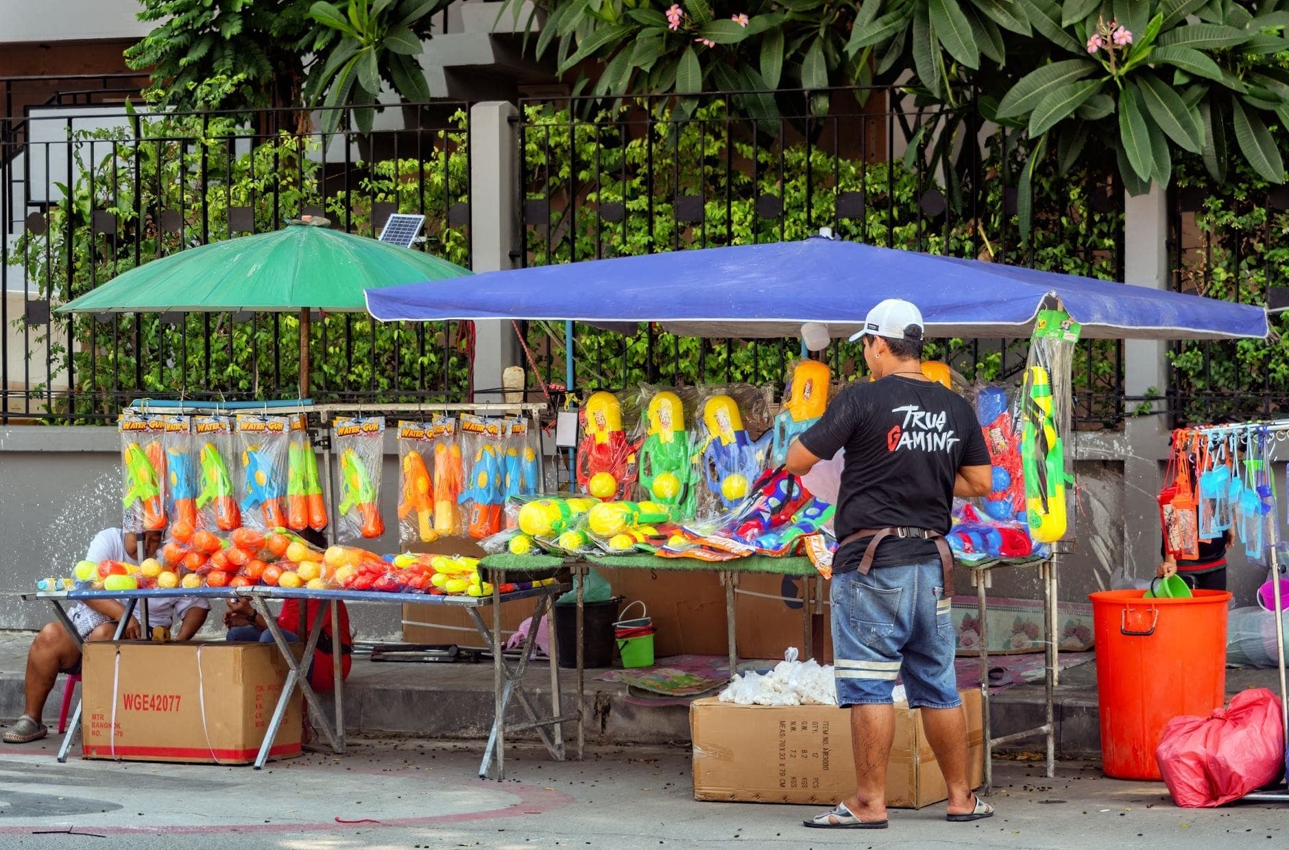 Chiang Mai'nin bir sokağında kurulmuş renkli Songkran su tabancası tezgahları; kovalar, su tabancaları ve gün ışığında festival hazırlıklarını gösteriyor.