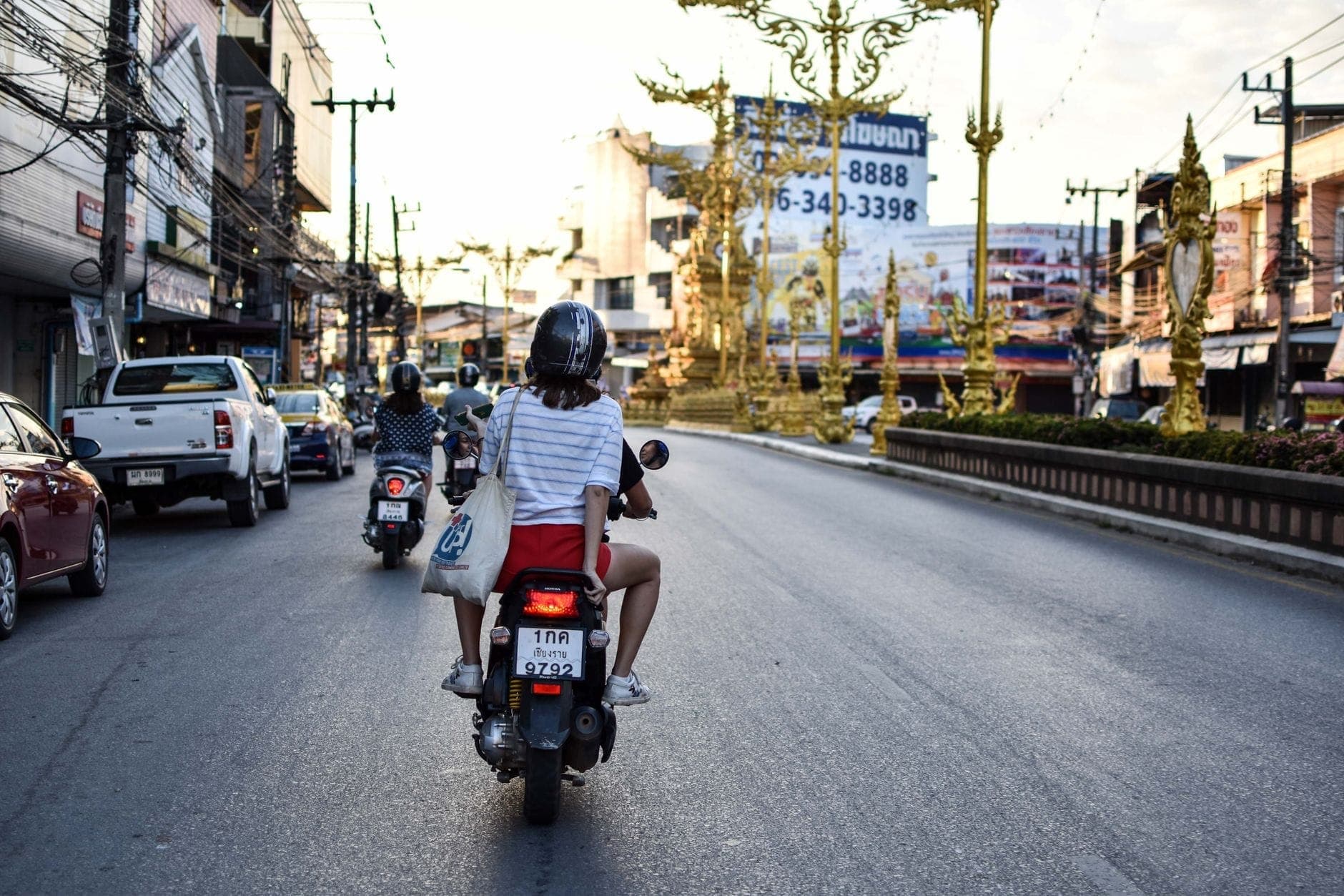 Roller und Motorräder fahren auf den berühmten goldenen Uhrturm von Chiang Rai in einer lebhaften Stadtstraßenszene zu.