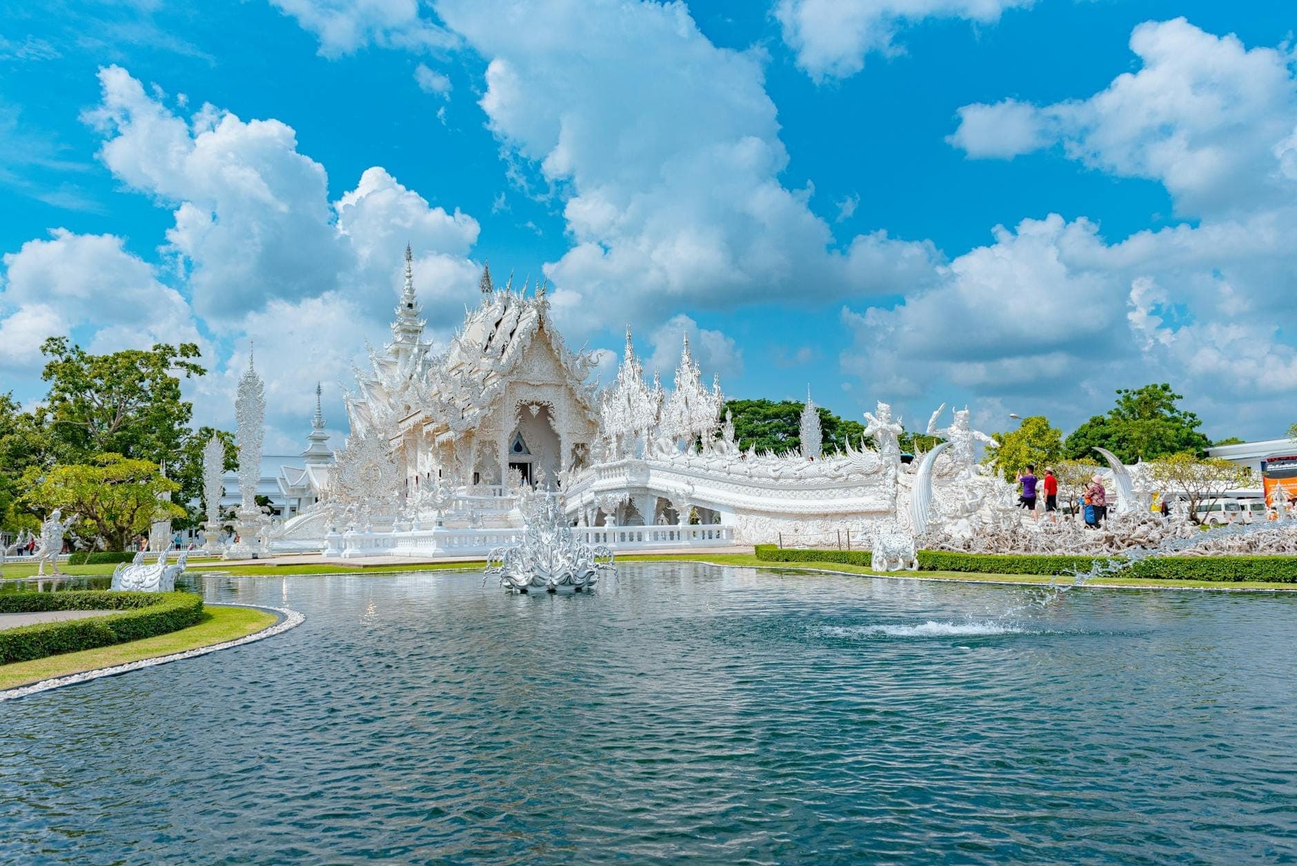 Der Weiße Tempel (Wat Rong Khun) in Chiang Rai, Thailand, mit seiner kunstvollen weißen Architektur und Brücke, die sich an einem sonnigen Tag in einem Teich spiegeln.