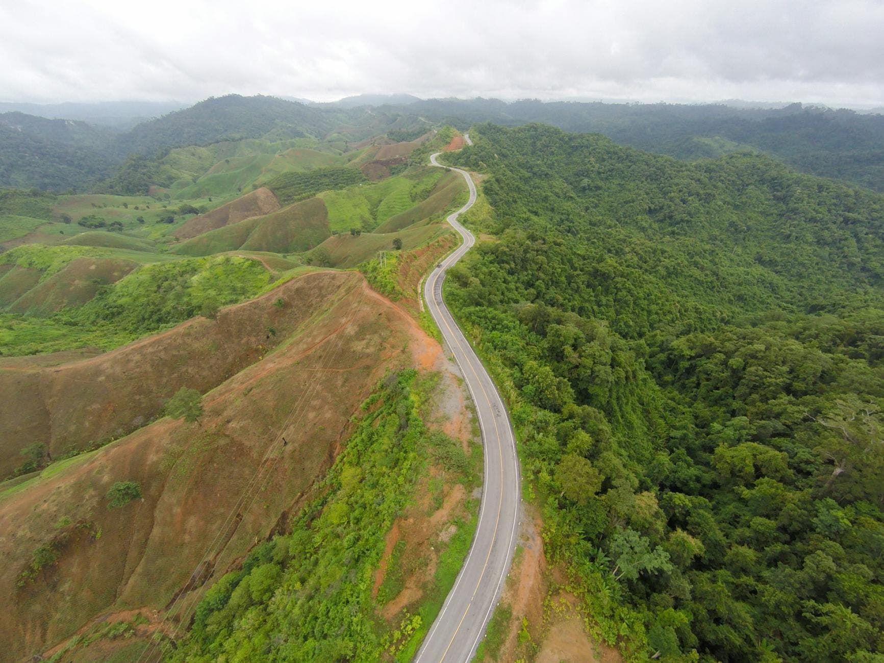 Una sinuosa carretera de montaña que atraviesa exuberantes colinas verdes bajo un cielo nublado, ilustrando la pintoresca pero tortuosa ruta hacia Pai.