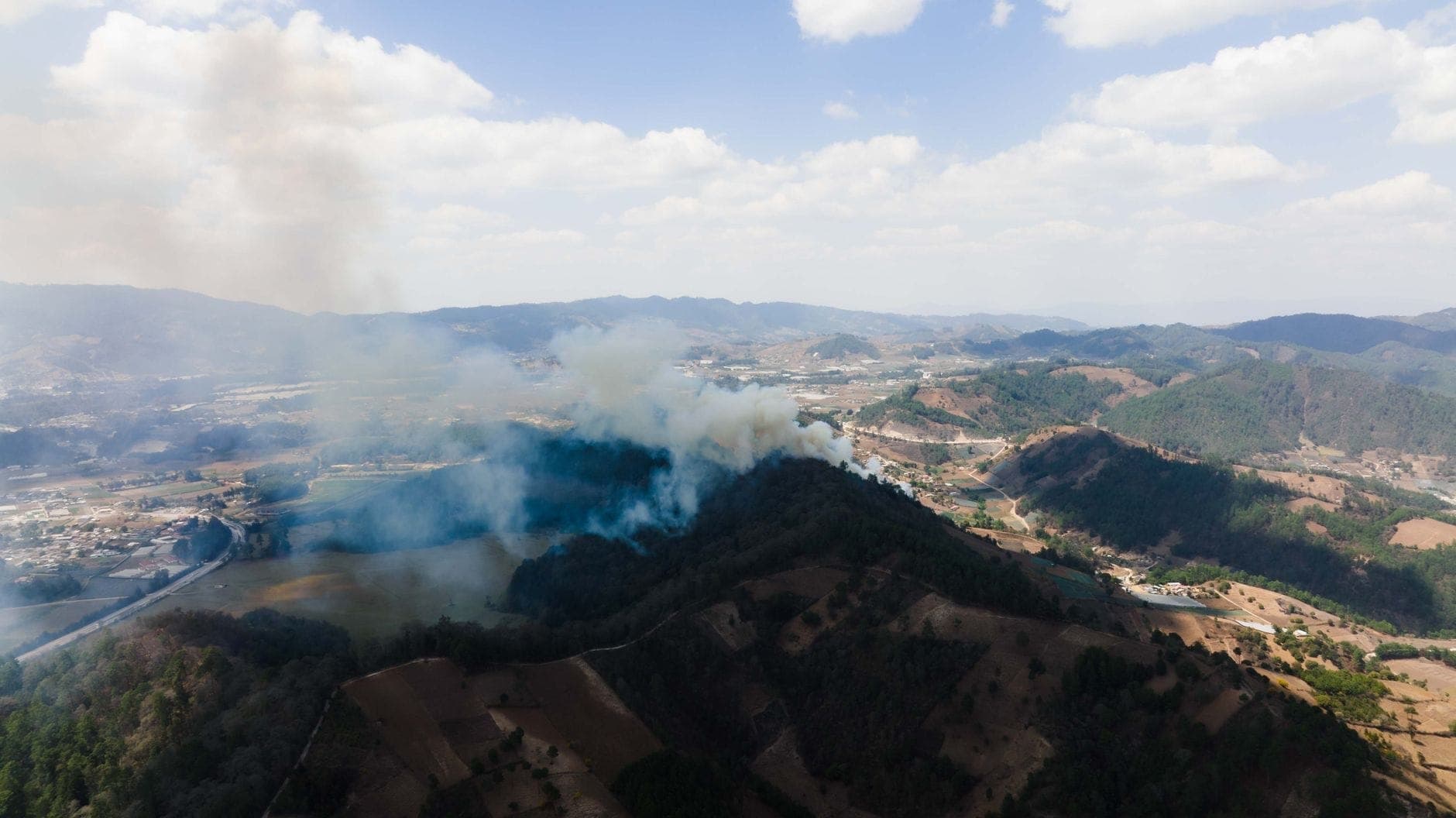Luftaufnahme der Hügel Nordthailands mit großen aufsteigenden Rauchwolken, die auf die Brandsaison in der Landschaft hinweisen.
