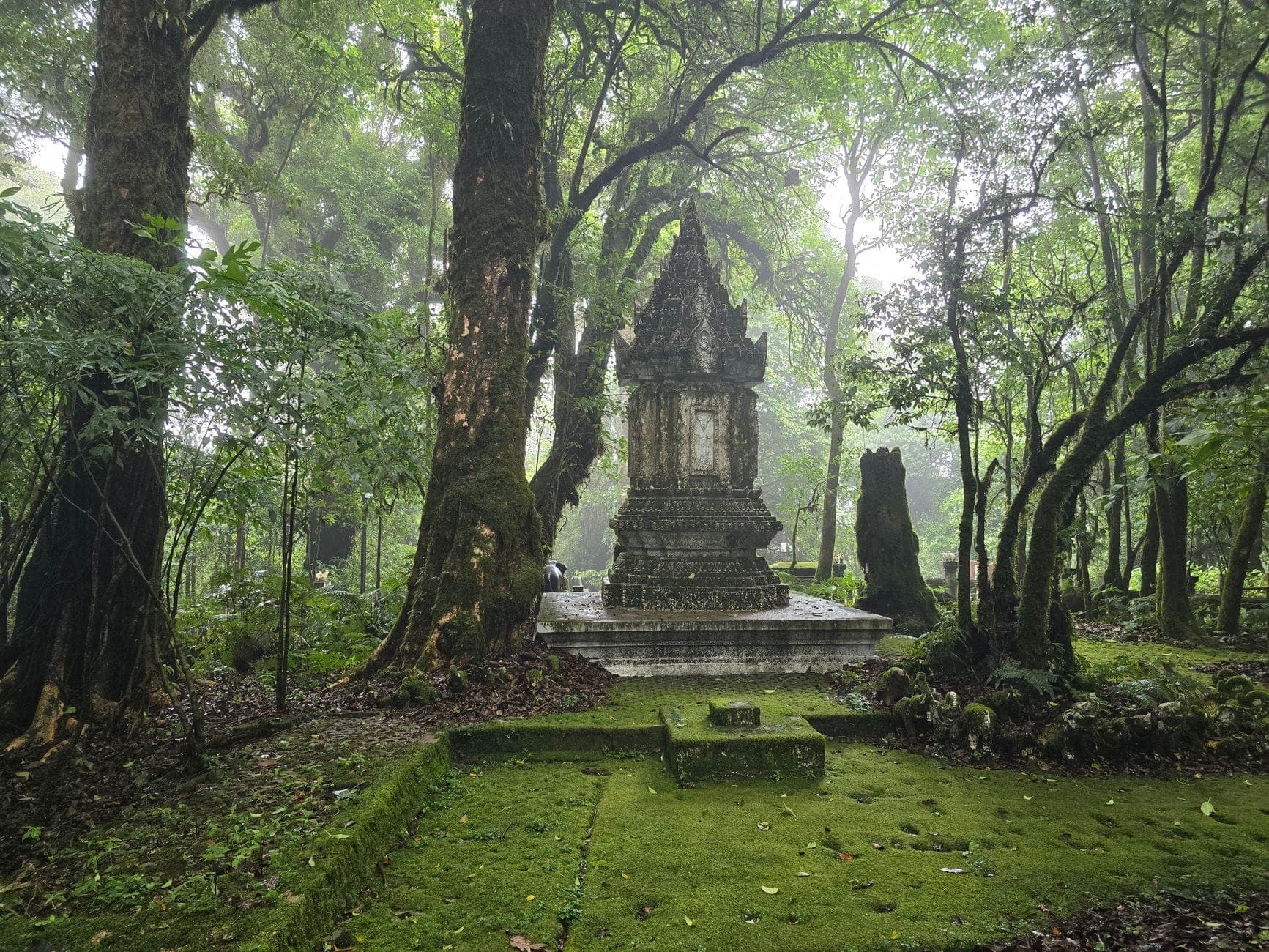 Moosbedecktes Steinmonument, umgeben von einem üppigen, dichten grünen Wald mit Nebel in der Luft nach dem Regen in Chiang Mai.
