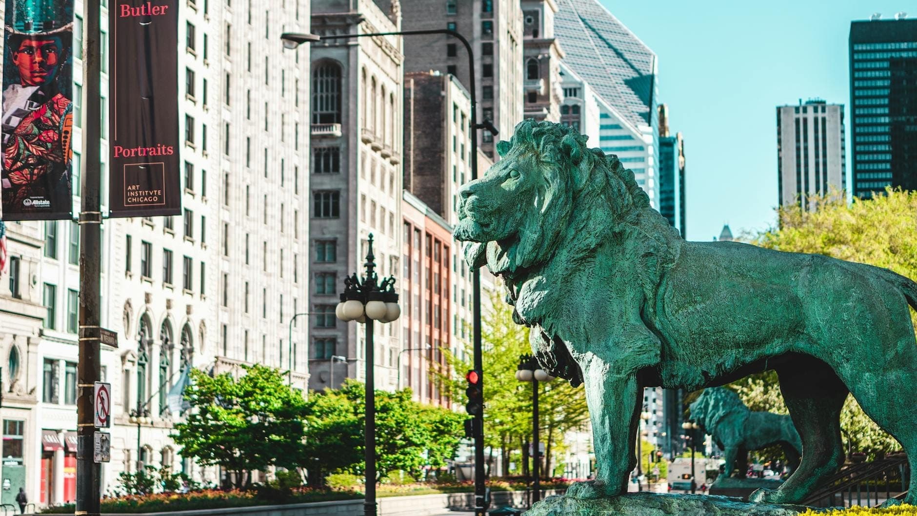 Iconic bronze lion statue outside the Art Institute of Chicago with Michigan Avenue and historic architecture in the background.