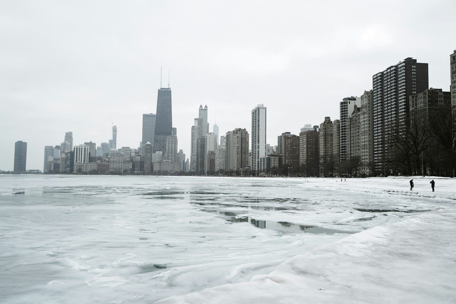 Skyline von Chicago mit Hochhäusern neben dem zugefrorenen, schneebedeckten Lake Michigan im Winter. Bedeckter Himmel und eisige Landschaft prägen die Szene.