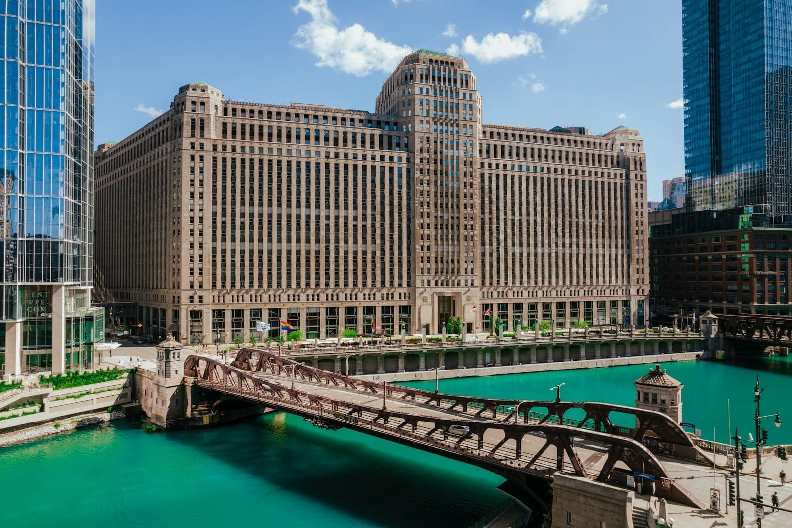 El edificio Merchandise Mart junto al río Chicago, con un puente y agua turquesa en primer plano bajo un cielo azul.