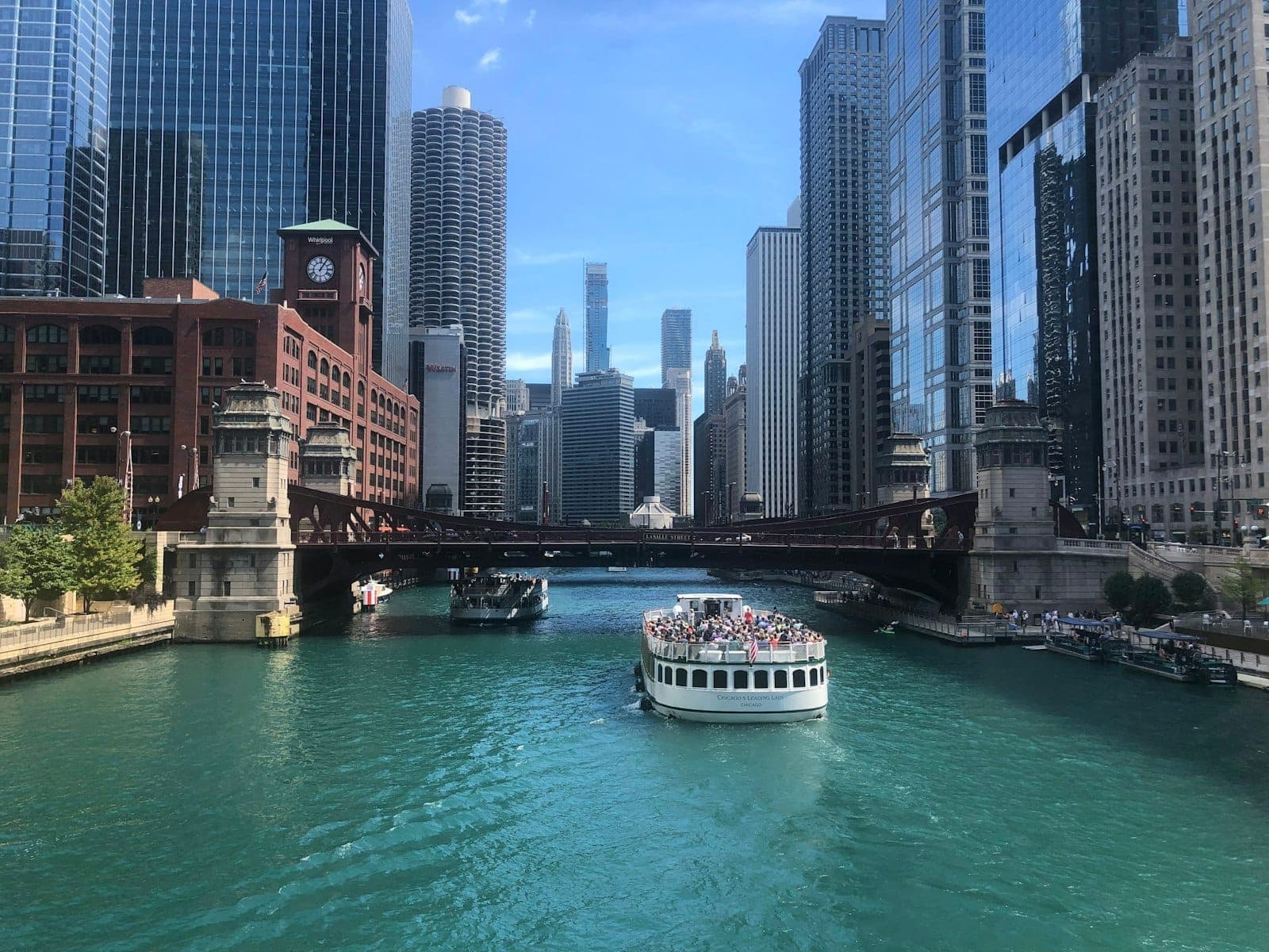 A tour boat cruises down the Chicago River surrounded by iconic skyscrapers and bridges, capturing the city’s famous architecture on a clear day.