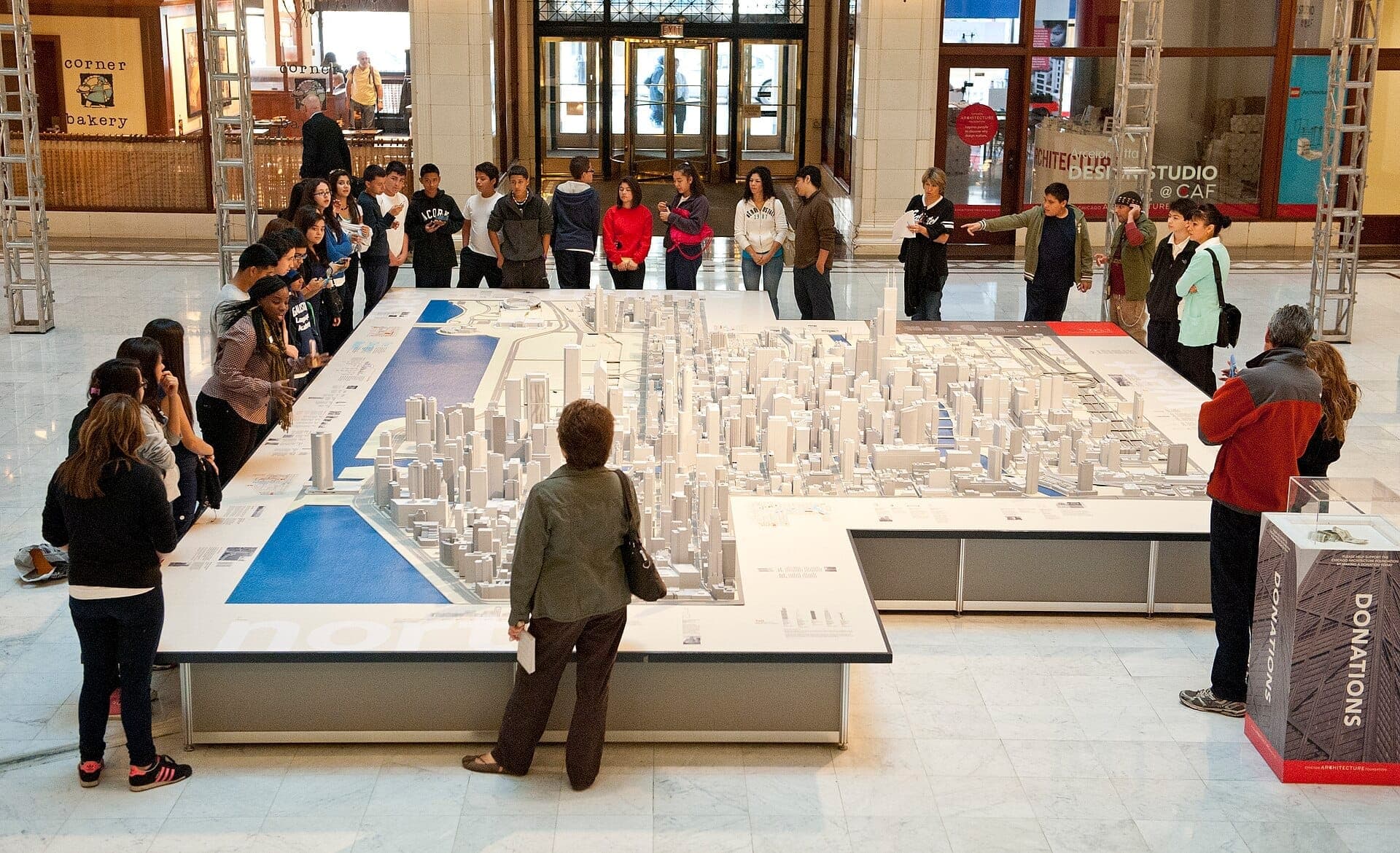 Visitors gather around an intricate scale model of Chicago at the Chicago Architecture Center, with natural light filling the spacious exhibition hall.