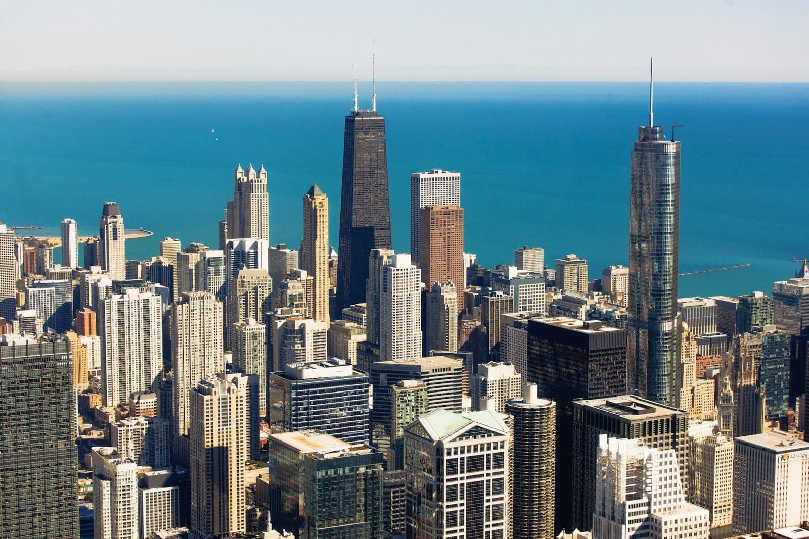 Aerial view of Chicago’s iconic downtown skyline with skyscrapers and Lake Michigan in the background on a clear sunny day.
