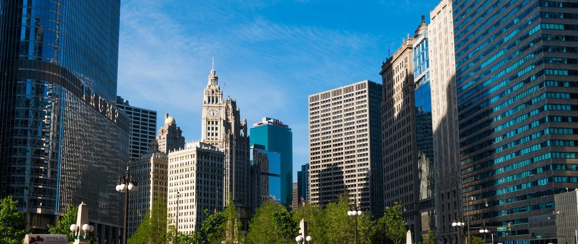 Vista diurna del paseo fluvial de Chicago con el Wrigley Building, la Tribune Tower y rascacielos modernos bajo un cielo azul despejado.