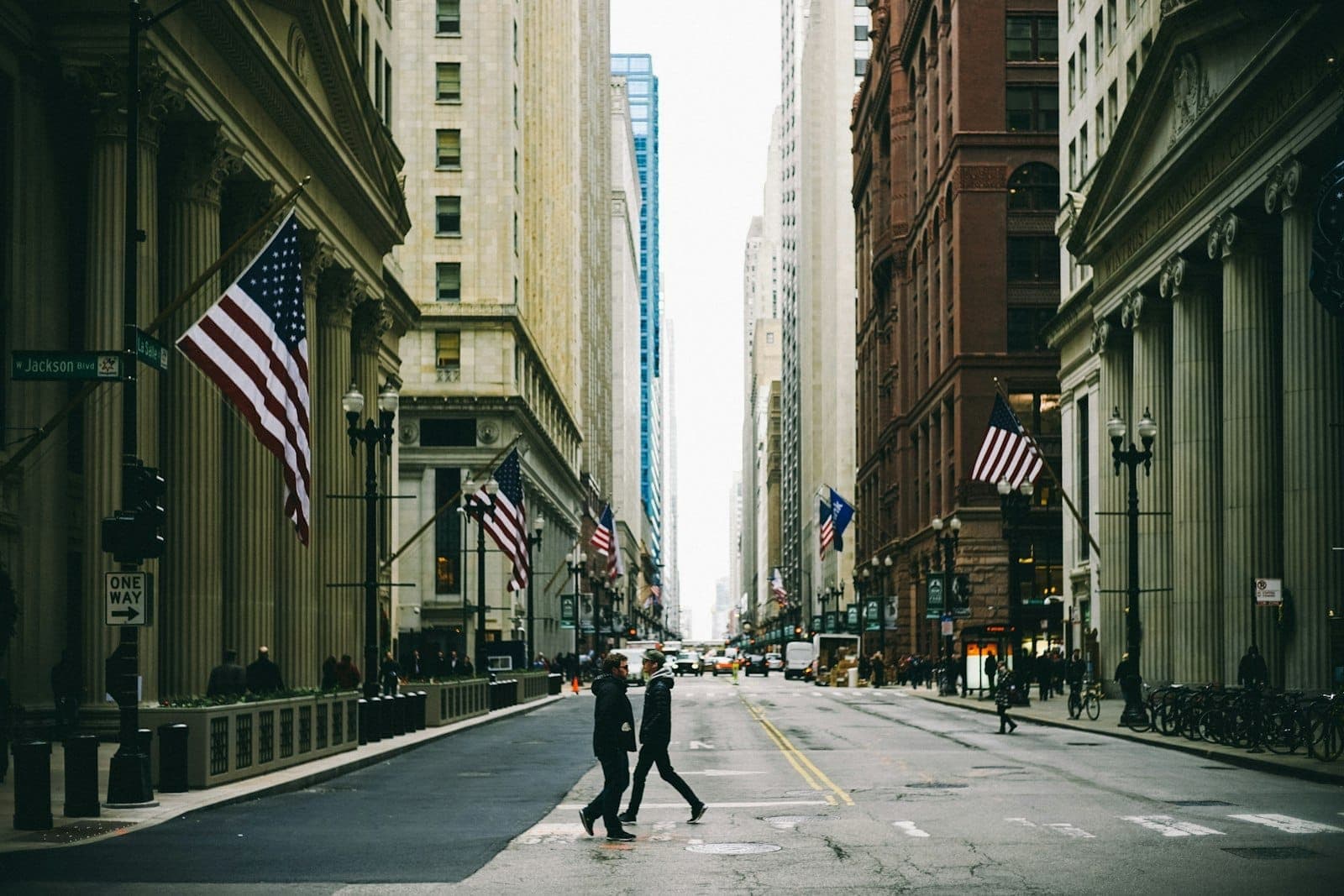 Vista de la calle en el Loop de Chicago con edificios históricos con columnas, banderas estadounidenses y personas cruzando en la intersección de LaSalle y Dearborn.