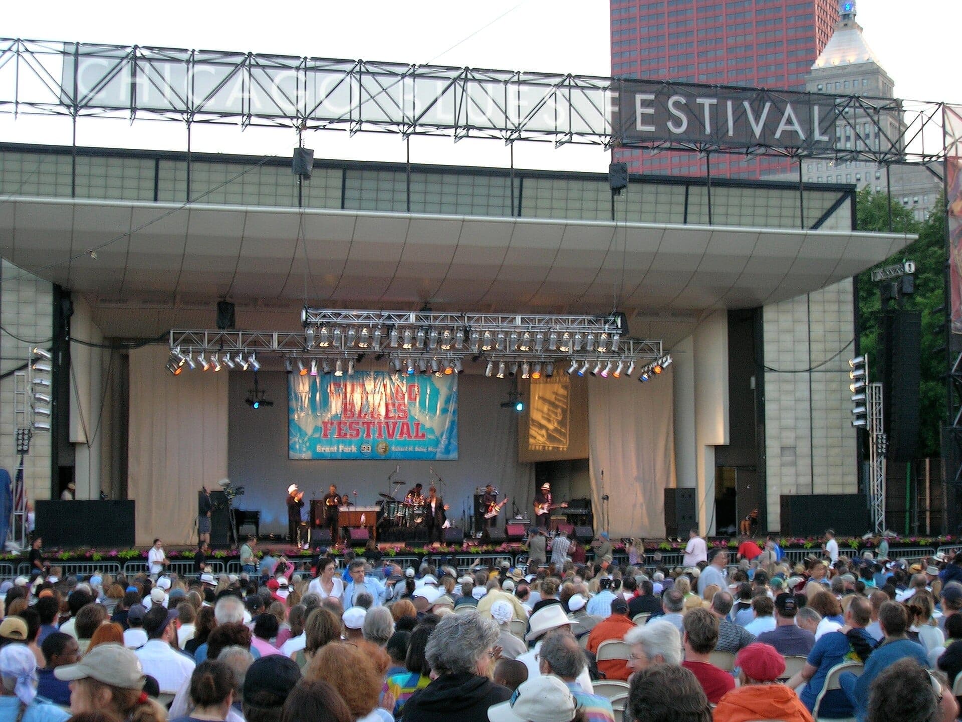 Eine große Menschenmenge versammelt sich im Millennium Park, um Musiker auf einer Freilichtbühne beim Chicago Blues Festival unter einem Festivalbanner zu beobachten.