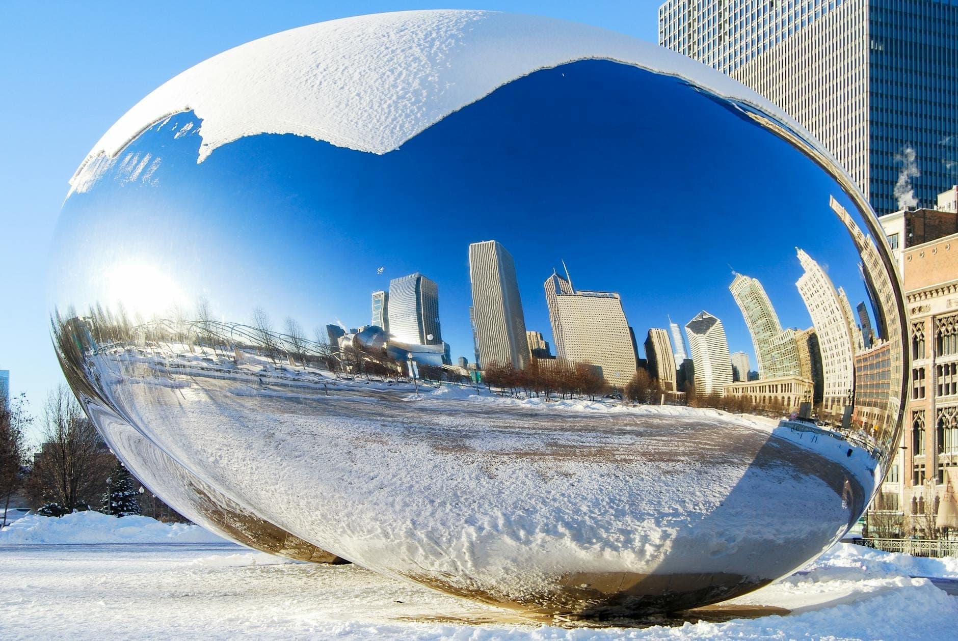 Cloud Gate sculpture, also known as 'The Bean,' covered in snow with Chicago skyscrapers reflected on its surface, surrounded by winter scenery in Millennium Park.