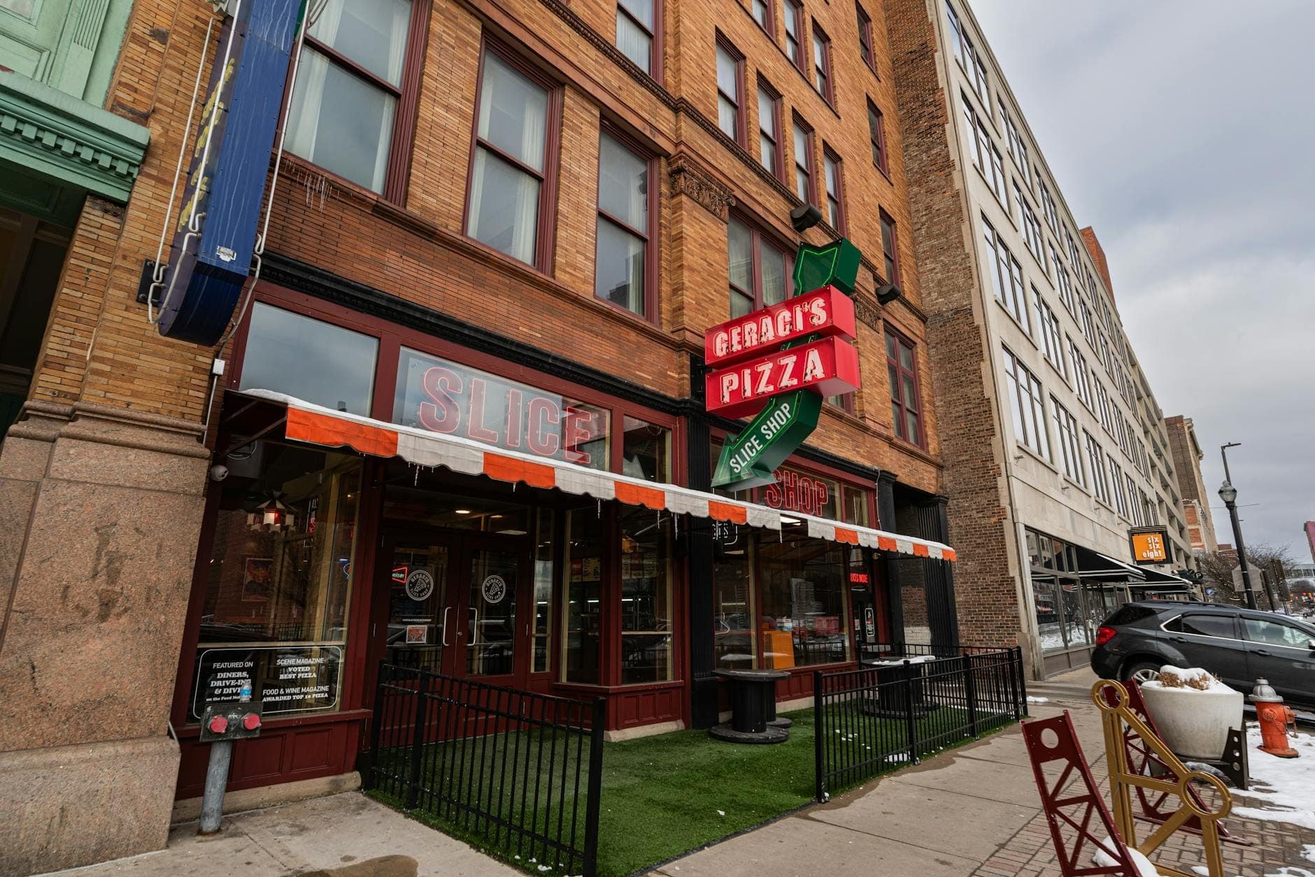 Street-level view of a pizza restaurant with red neon sign, large windows, and historic brick Chicago building