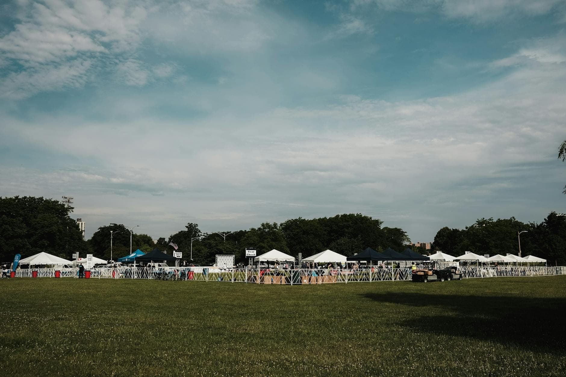 Rows of white festival tents set up on grassy field with people walking, under blue skies; typical scene at outdoor food festivals in Chicago.
