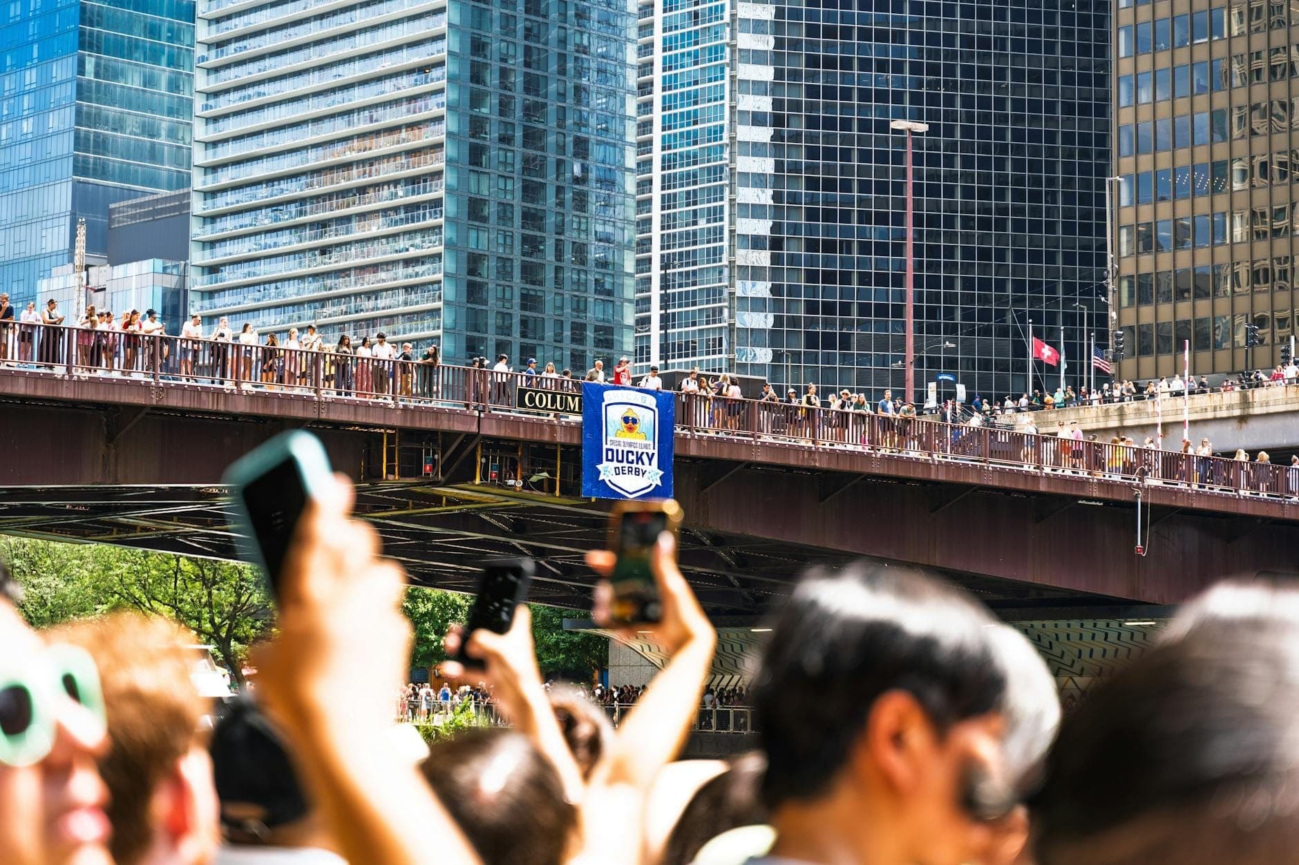 Đám đông mùa hè tập trung trên một cây cầu bắc qua Chicago River với các tòa nhà chọc trời khu trung tâm ở phía sau vào một ngày nắng đẹp.