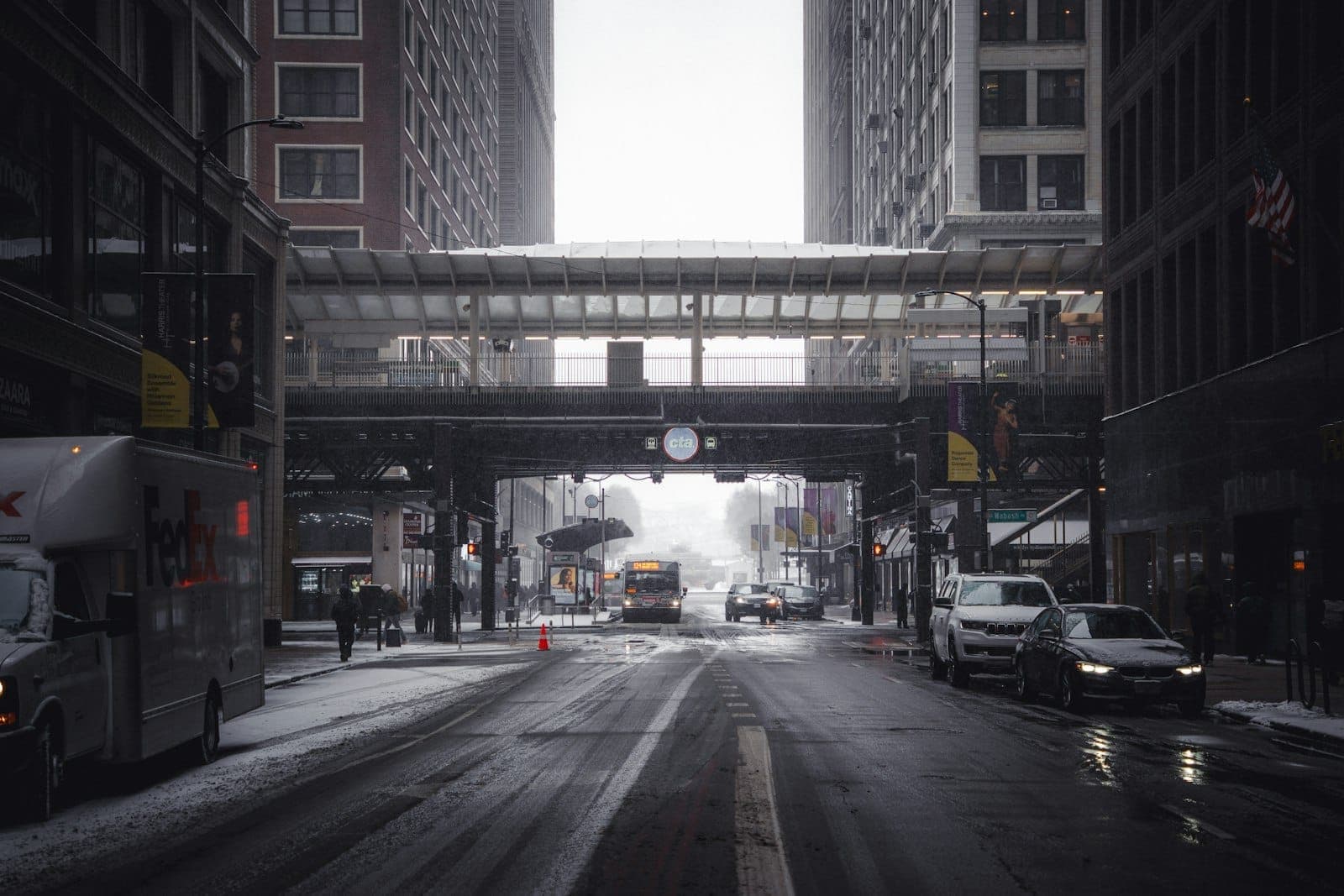 Snowy downtown Chicago street with cars, buses, and the elevated CTA 'L' train tracks overhead in winter.
