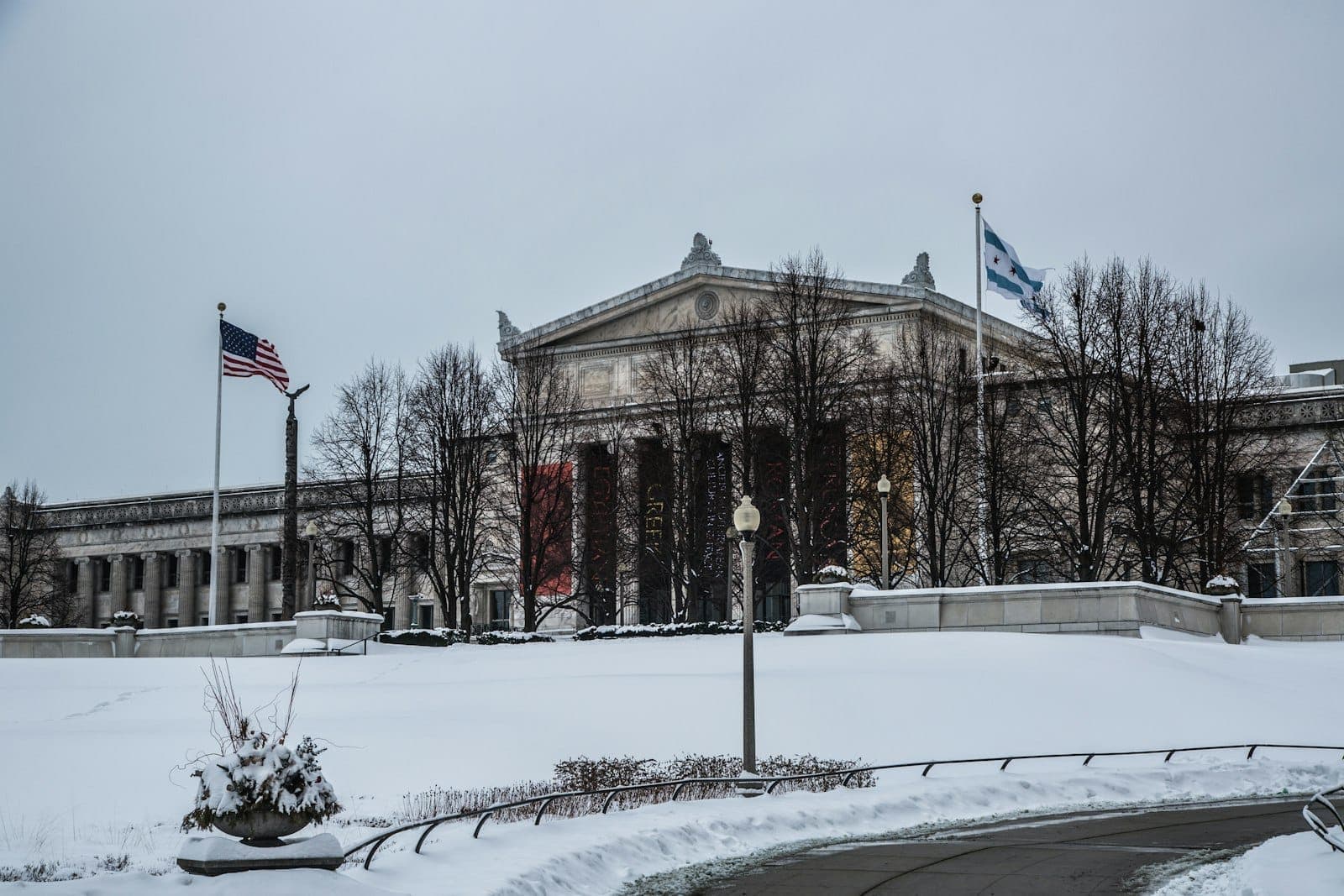 Winter view of the Art Institute of Chicago with snow on the ground and bare trees, flags flying in front.