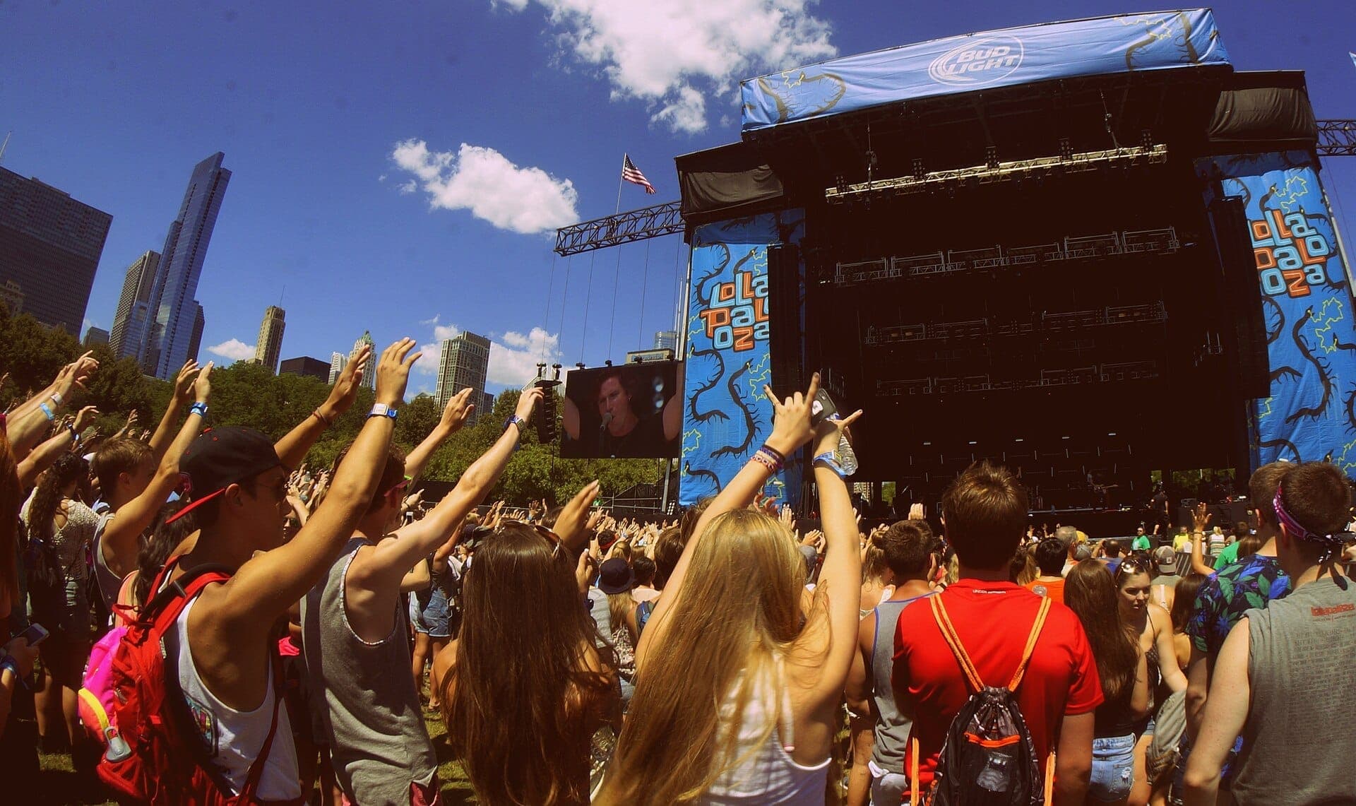 Đám đông lớn tập trung trước sân khấu Lollapalooza tại Grant Park, Chicago, với các tòa nhà chọc trời của thành phố và bầu trời xanh tươi sáng ở phía sau.