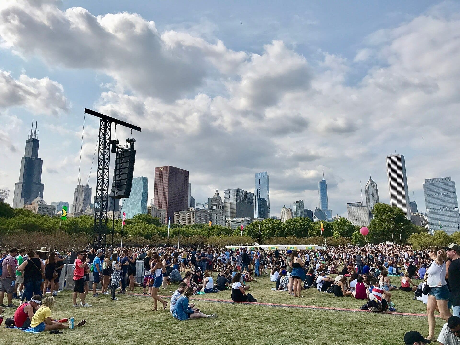 Đám đông lớn tập trung tại Grant Park cho Lollapalooza, với đường chân trời Chicago và Willis Tower hiện ra dưới bầu trời có mây rải rác.