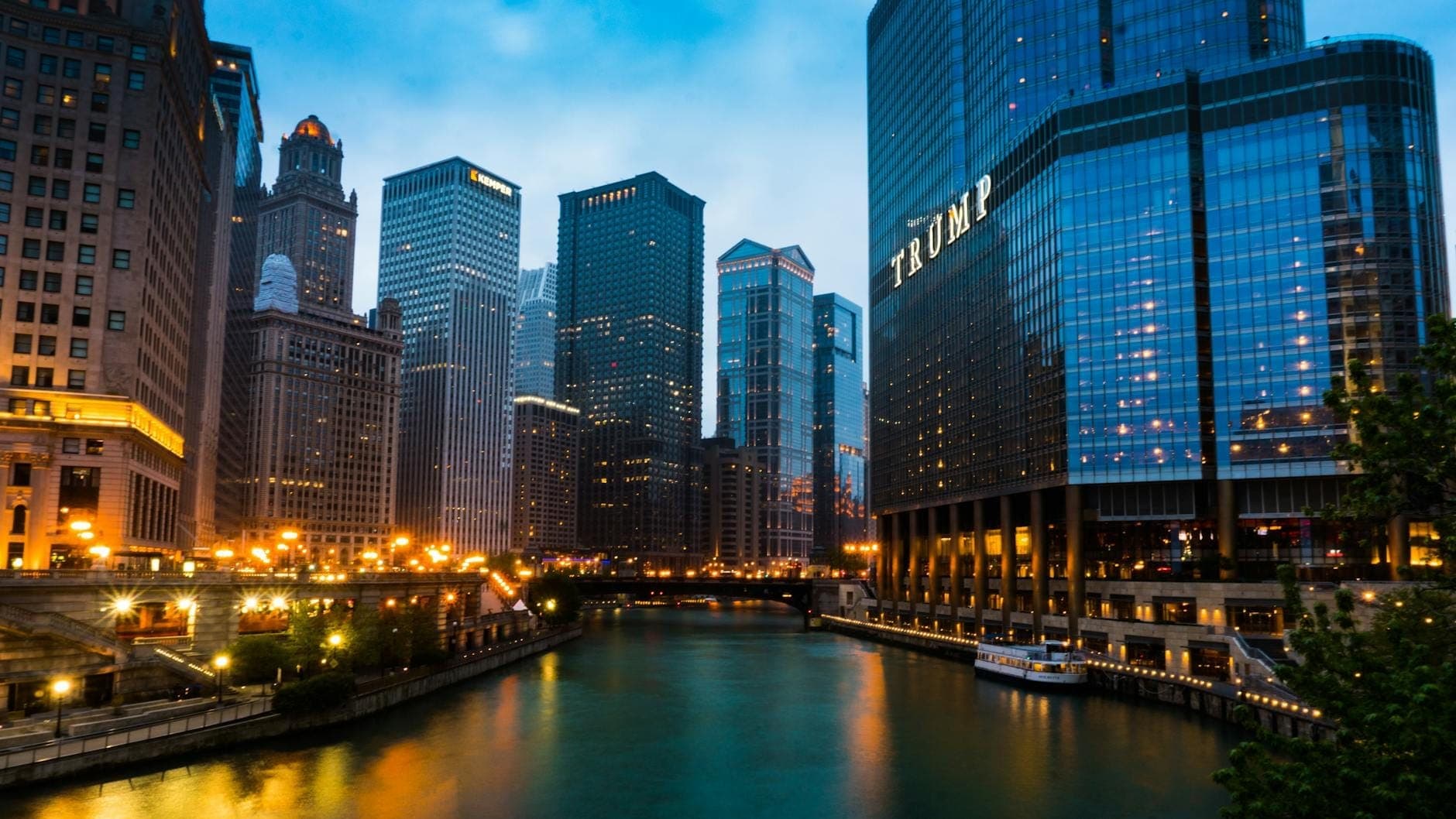 Chicago Riverwalk at dusk with luxury hotels and modern skyscrapers including the Trump Tower reflecting on the water.