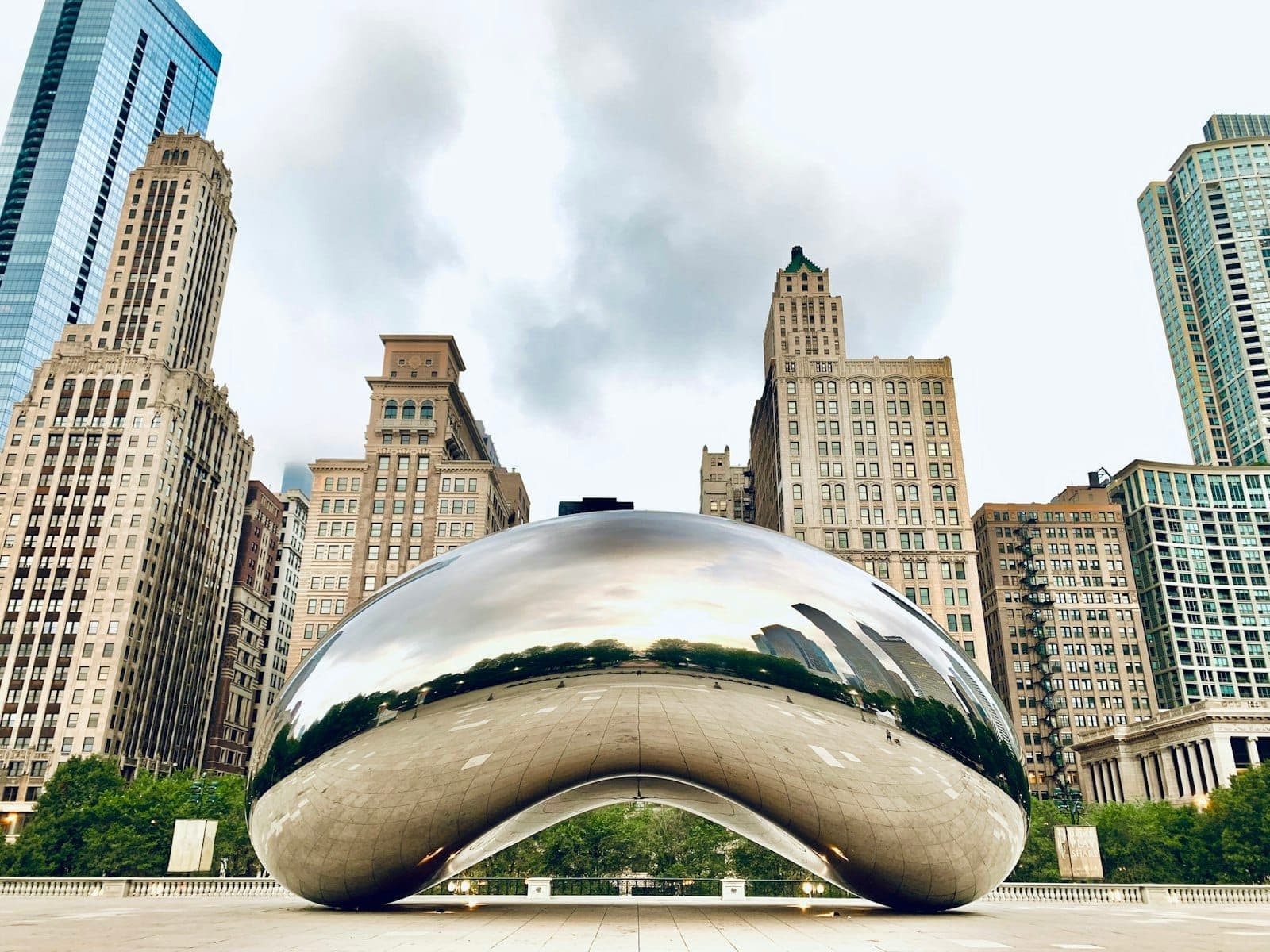 Cloud Gate sculpture in Millennium Park, Chicago, with surrounding skyscrapers and clear sky in the background.