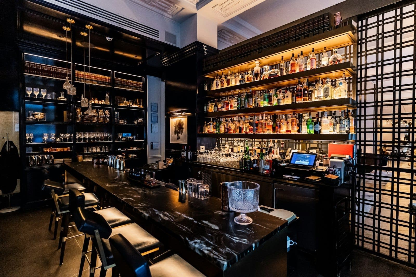Elegant bar interior with backlit shelves of liquor bottles, marble countertop, and modern barstools in a stylish Chicago venue.