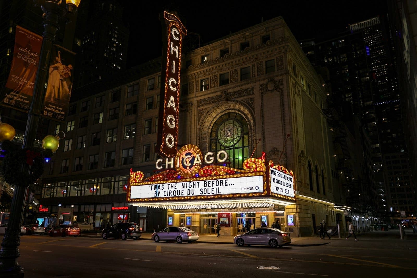 The iconic Chicago Theatre marquee lit up at night with cars parked along the street below and people walking nearby.