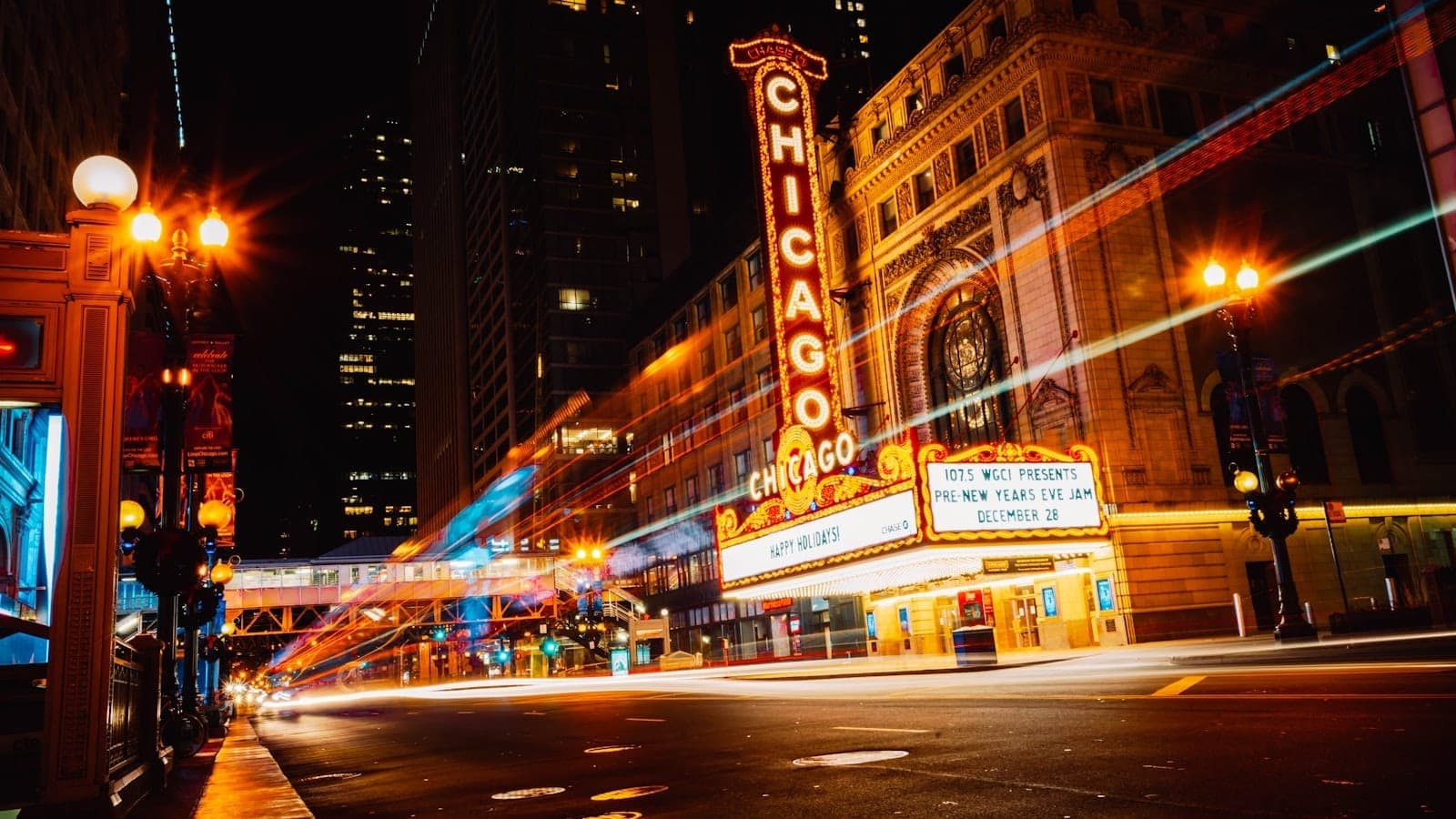Vibrant night scene of the iconic Chicago Theatre, neon lights glowing, with light trails from cars and surrounding city high-rises in the background.