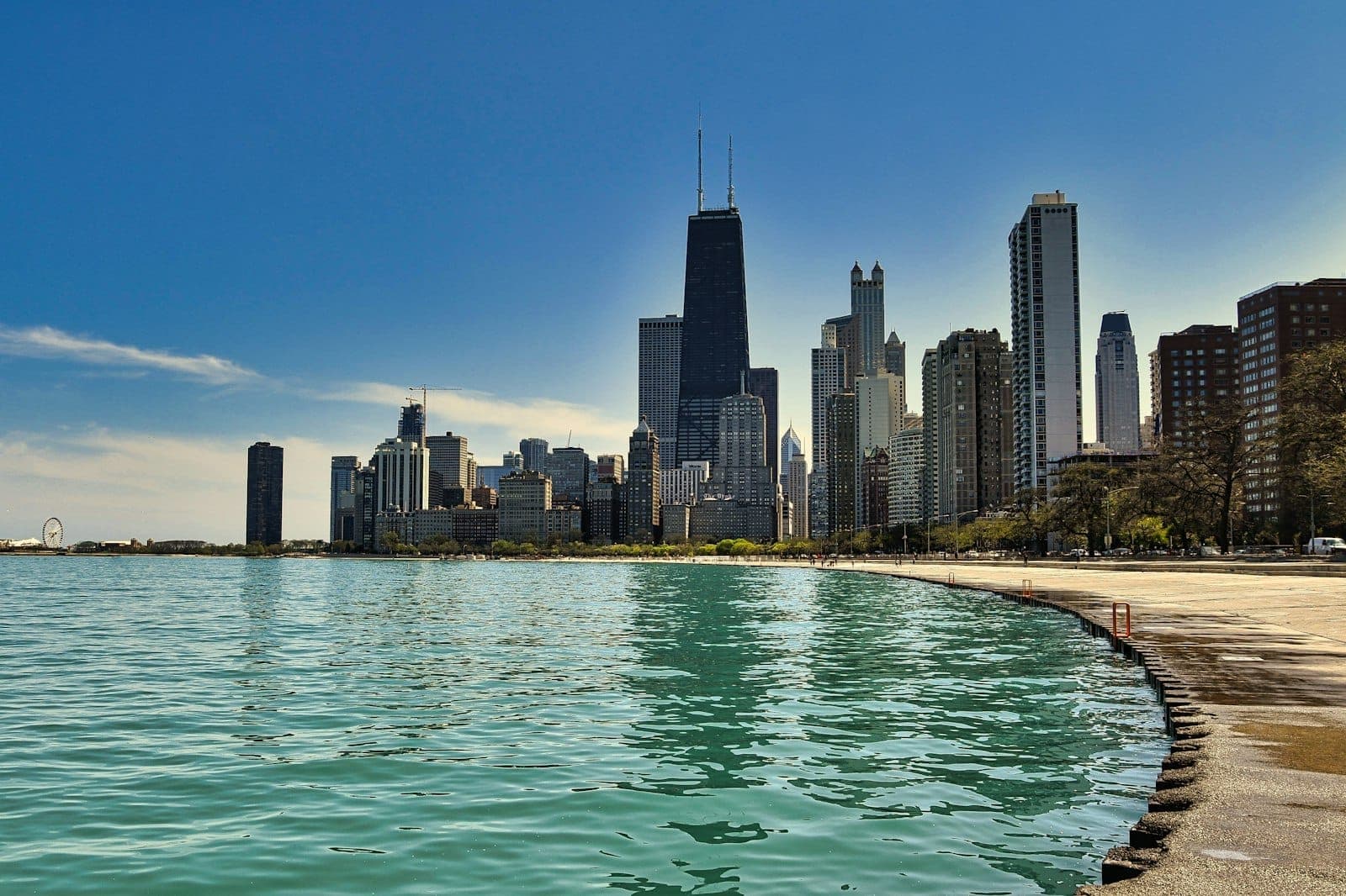 Chicago skyline viewed from the lakeshore, bright sunny day with calm water and iconic skyscrapers under a clear blue sky.