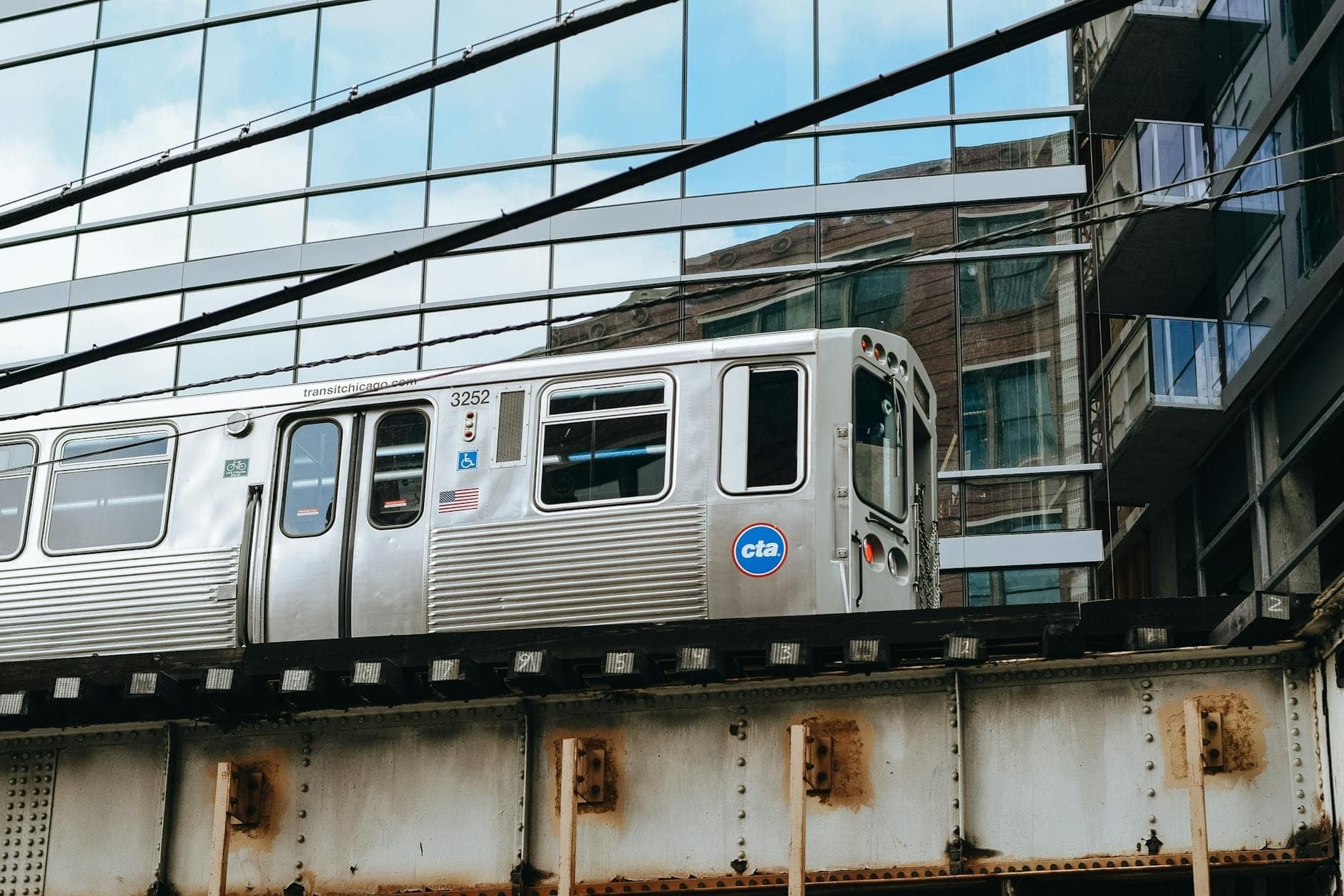 Elevated CTA train riding on tracks in front of modern glass building in Chicago, showcasing affordable public transit downtown.
