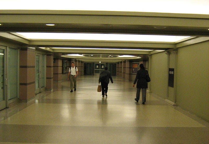 Wide, well-lit corridor inside the Chicago Pedway, with three people walking along polished floors and glass doors lining the walls.