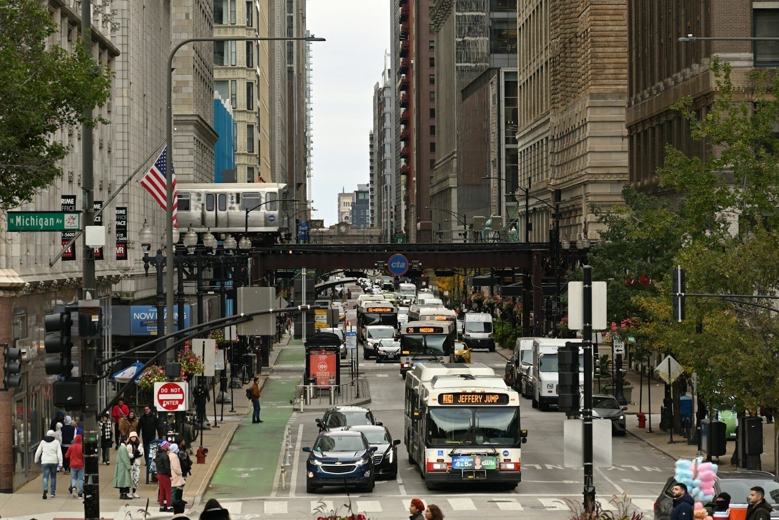 Busy Chicago street scene showing pedestrians, buses, and trains in the downtown Loop area with tall buildings and traffic.
