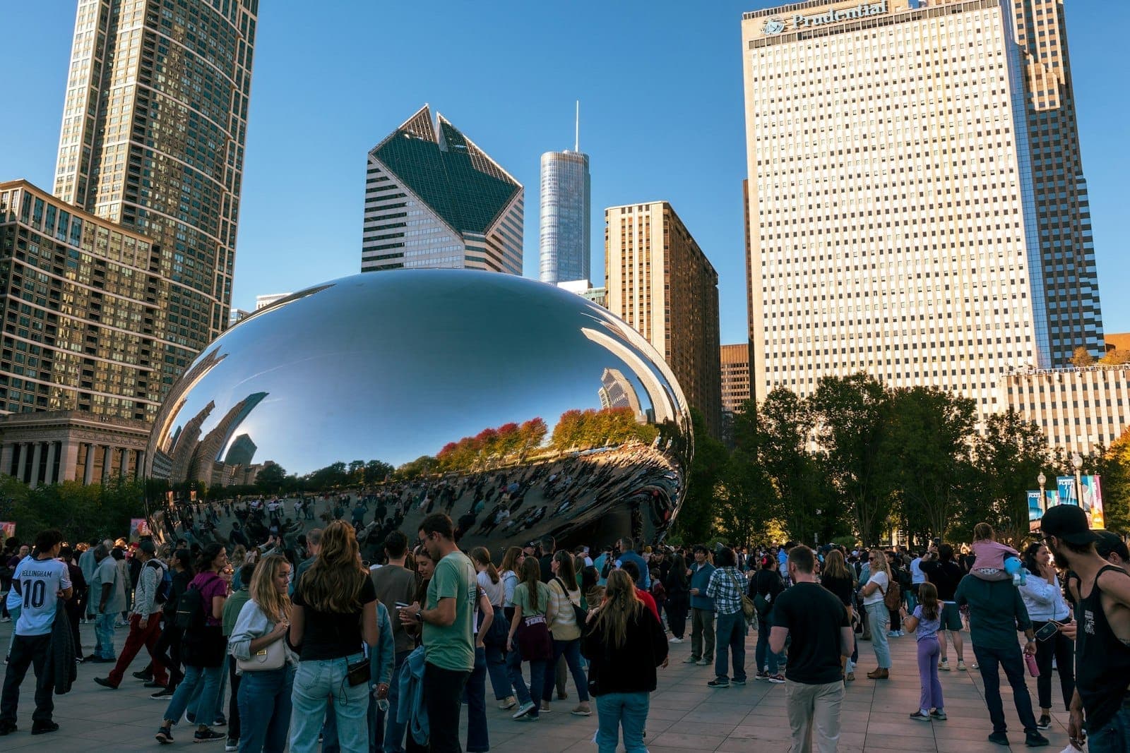 Crowds of tourists gathered around Chicago’s Cloud Gate sculpture in Millennium Park with city skyscrapers in the background on a sunny day.