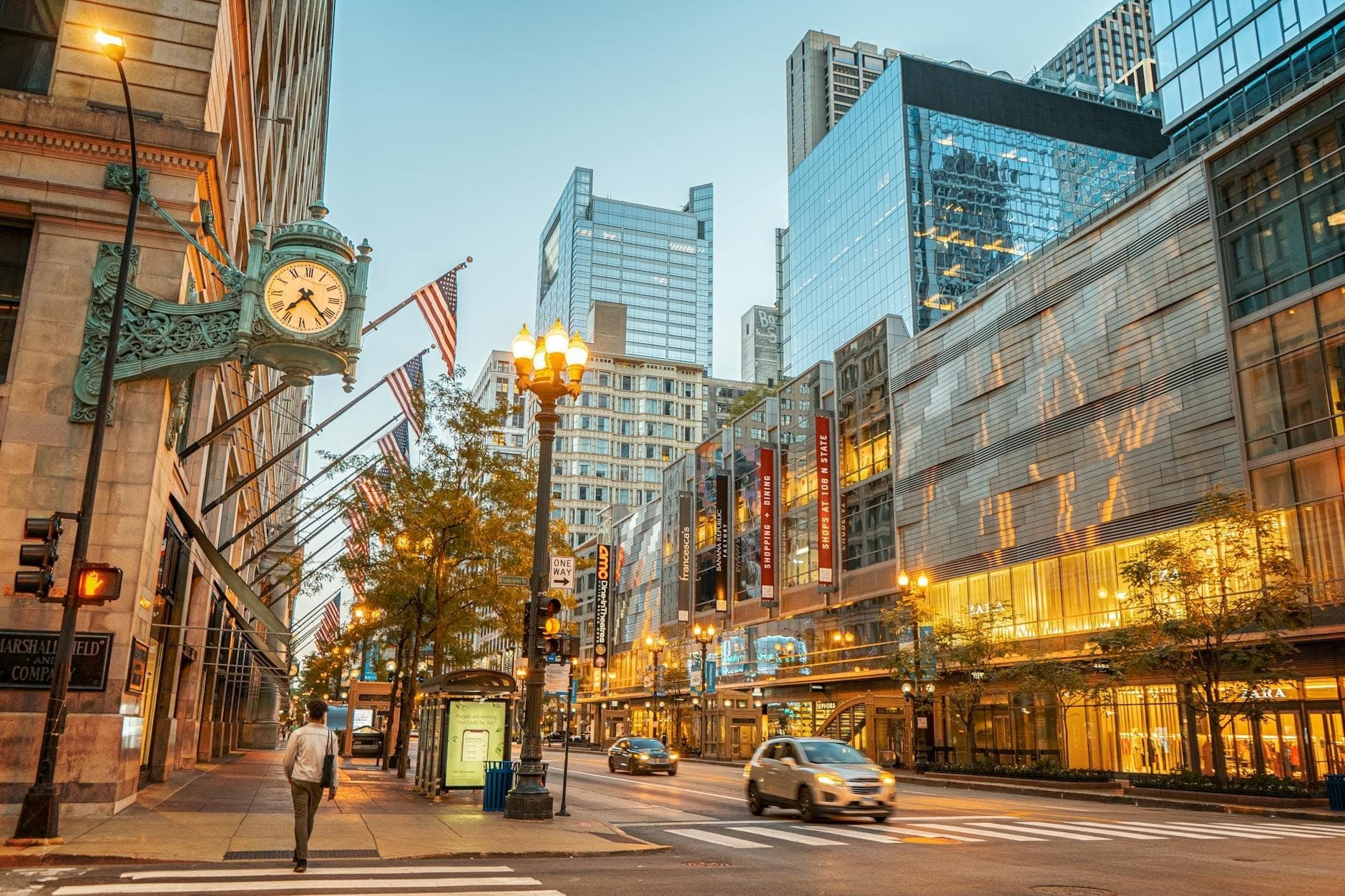 Downtown Chicago’s State Street with Marshall Field’s clock, Macy's, flags, modern glass buildings, and a few people and cars on the street.