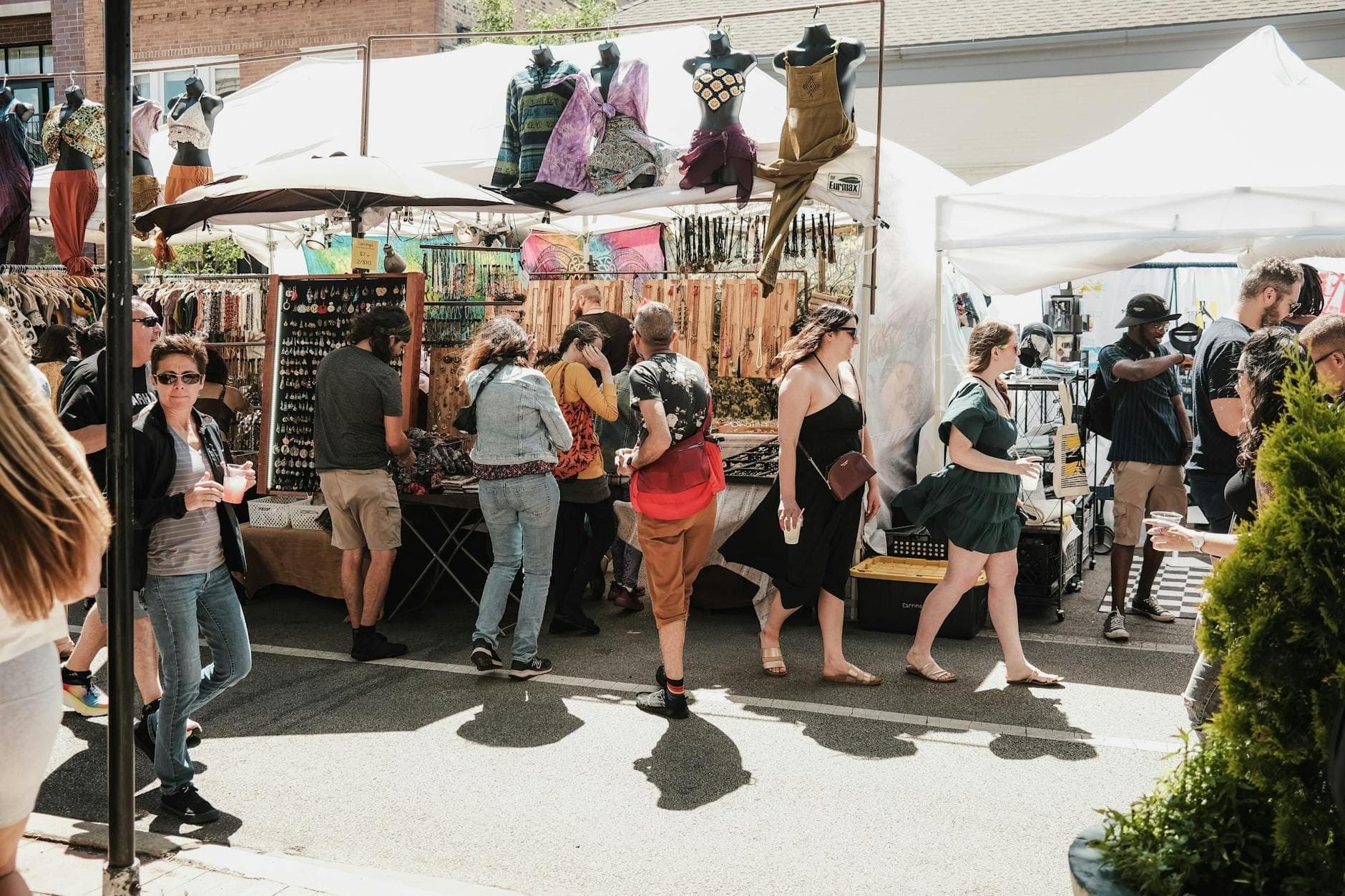 Outdoor market in Chicago with people browsing stalls selling clothing, jewelry, and crafts under white tents on a sunny day.
