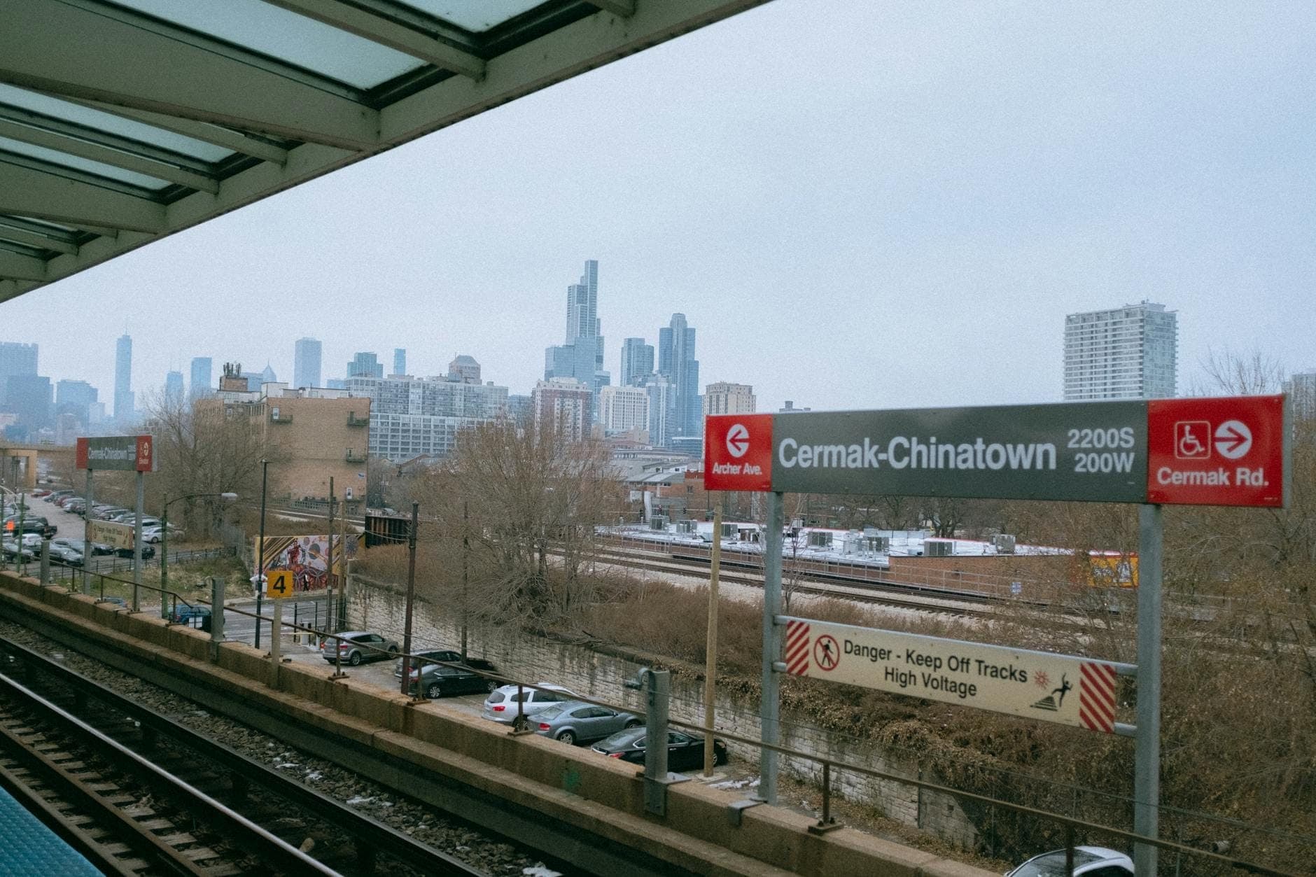 Chicago CTA L train platform at Cermak-Chinatown station with city skyline in background and transit signs visible.