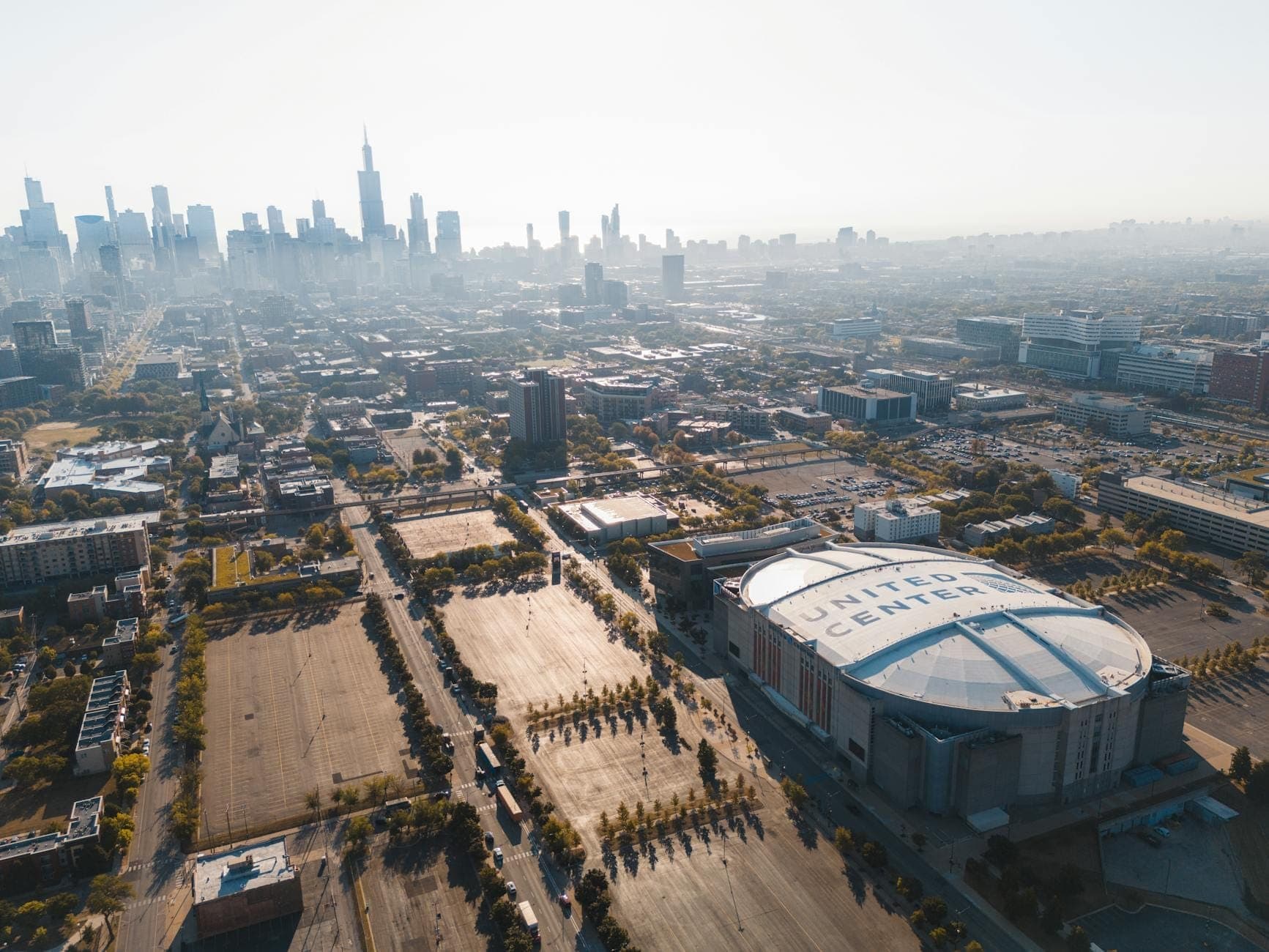 Aerial view of Chicago skyline with the United Center arena prominently in the foreground, surrounded by city buildings and parking lots.