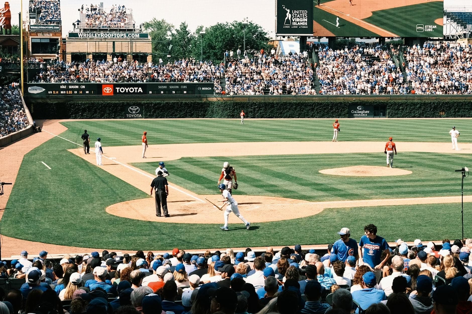 Packed crowd at Wrigley Field watching a baseball game, with batter at home plate and classic outfield ivy visible.