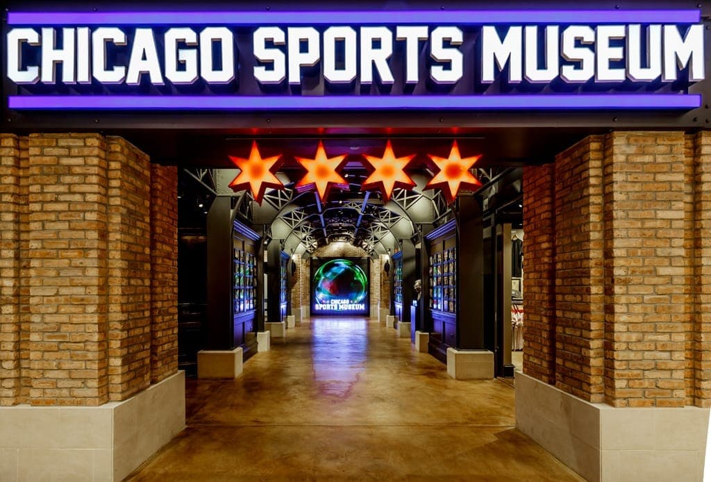 Entryway to the Chicago Sports Museum with illuminated sign, glowing Chicago stars, exposed brick walls, and sports displays along the hallway.