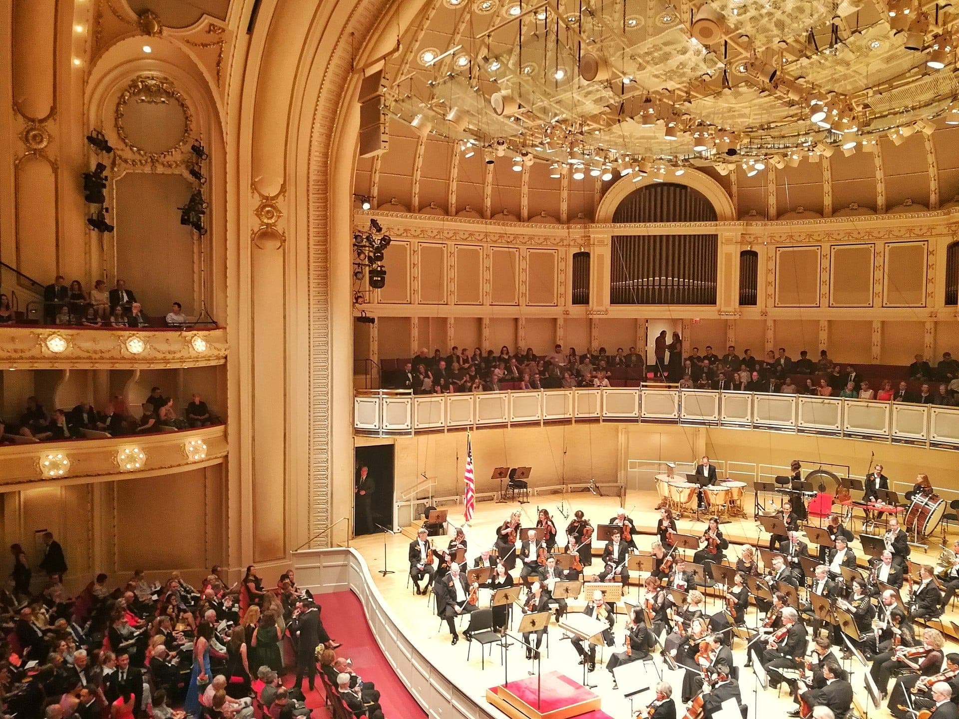 Orchester auf der Bühne des Chicago Symphony Center, umgeben von einem goldenen Auditorium, hohen Decken und einem Publikum, das den prunkvollen Konzertsaal füllt.