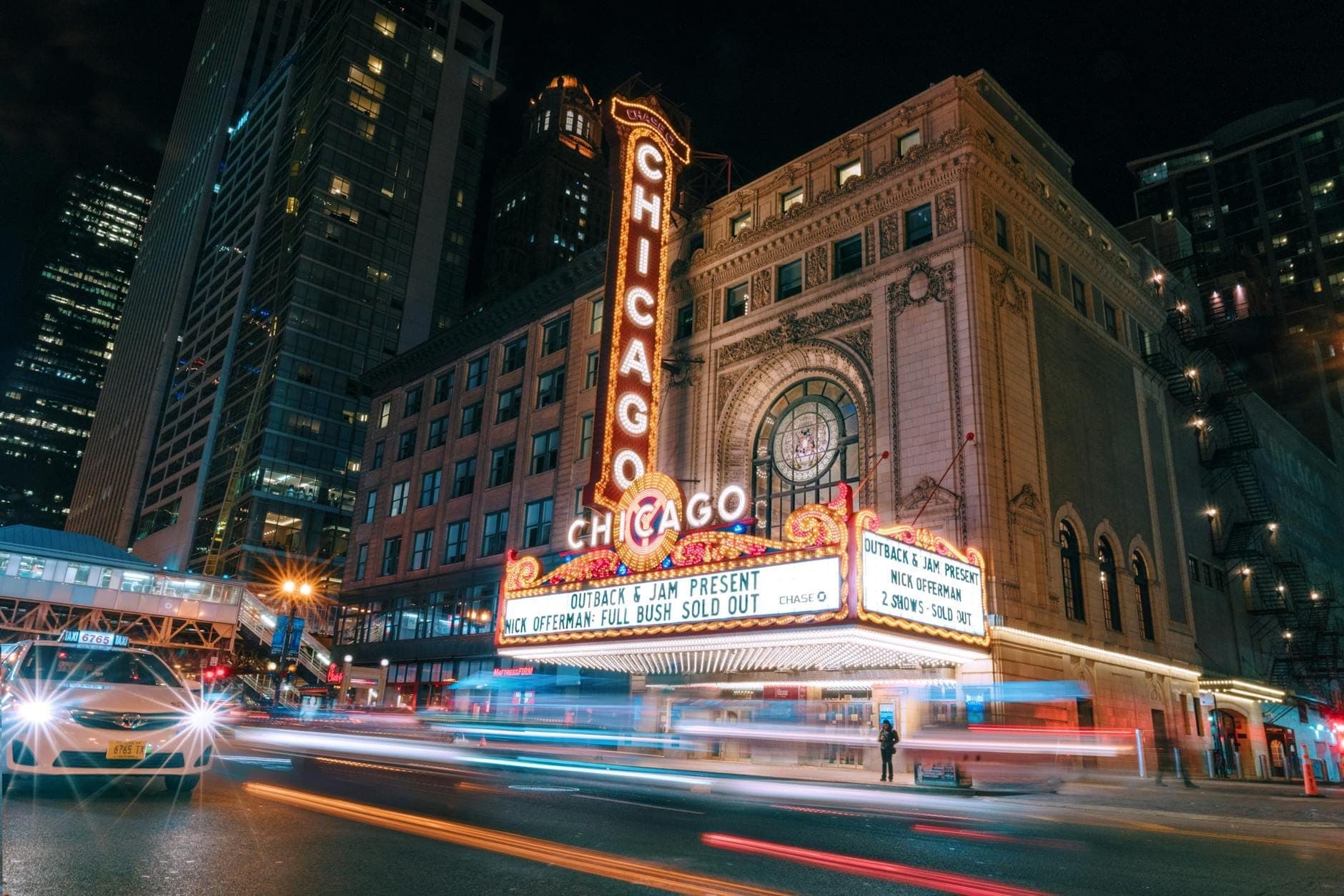 Nächtliche Ansicht des ikonischen beleuchteten Marquees des Chicago Theatre mit umliegenden Gebäuden der Innenstadt und Straßenverkehr im Loop.