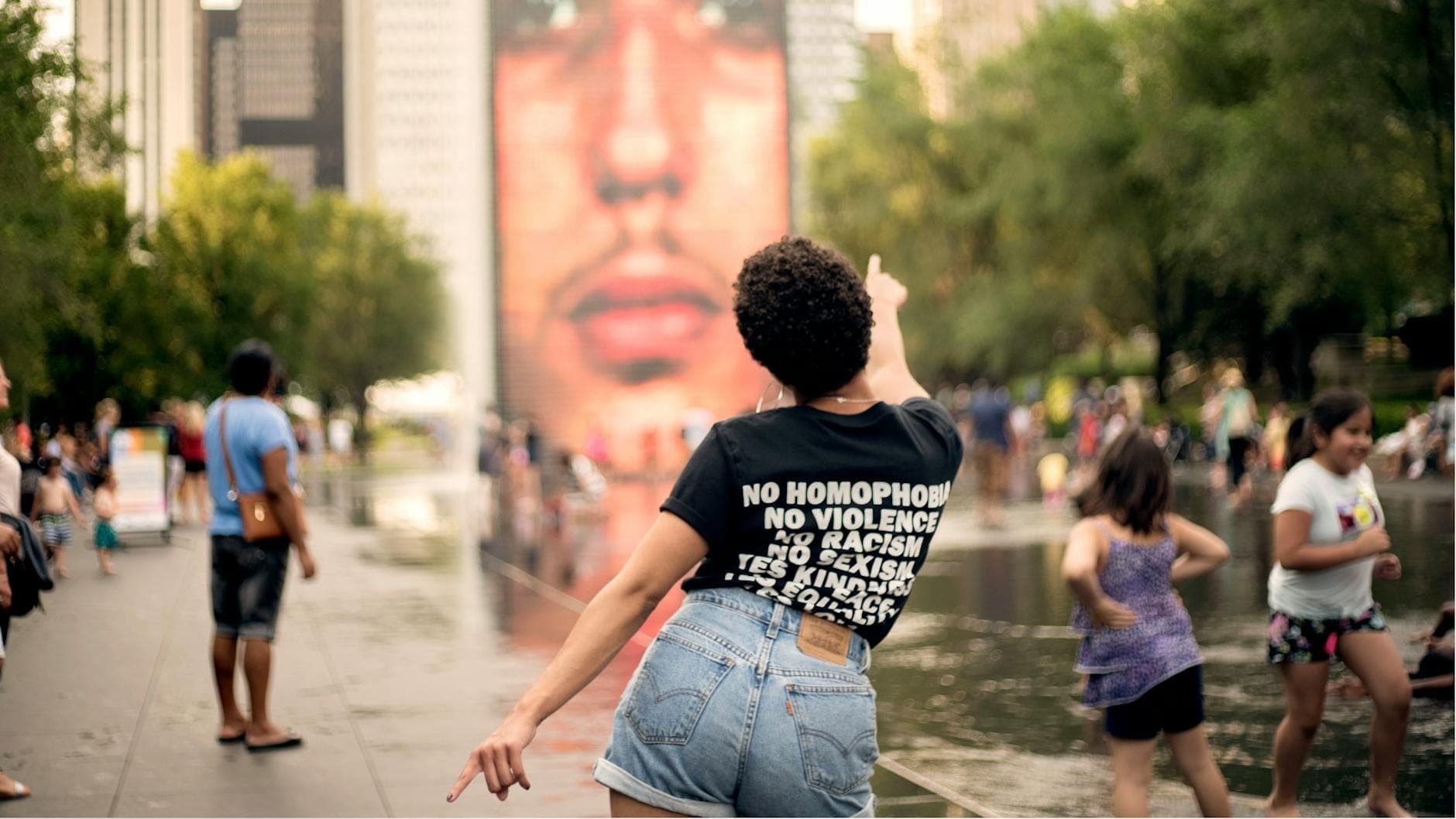 Menschen, die an der Crown Fountain im Millennium Park in Chicago spielen und die Wasserspiele genießen, umgeben von Bäumen und Hochhäusern.