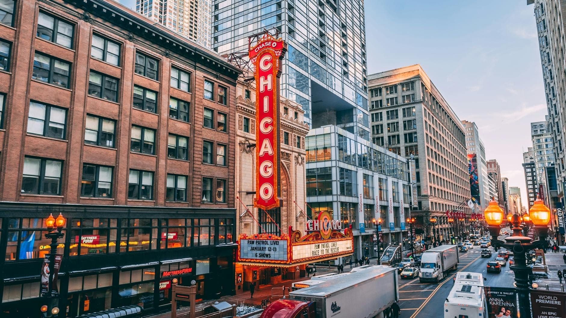 Daytime view of the Chicago Theatre’s iconic vertical neon marquee on State Street, surrounded by busy city traffic and high-rise buildings in downtown Chicago.