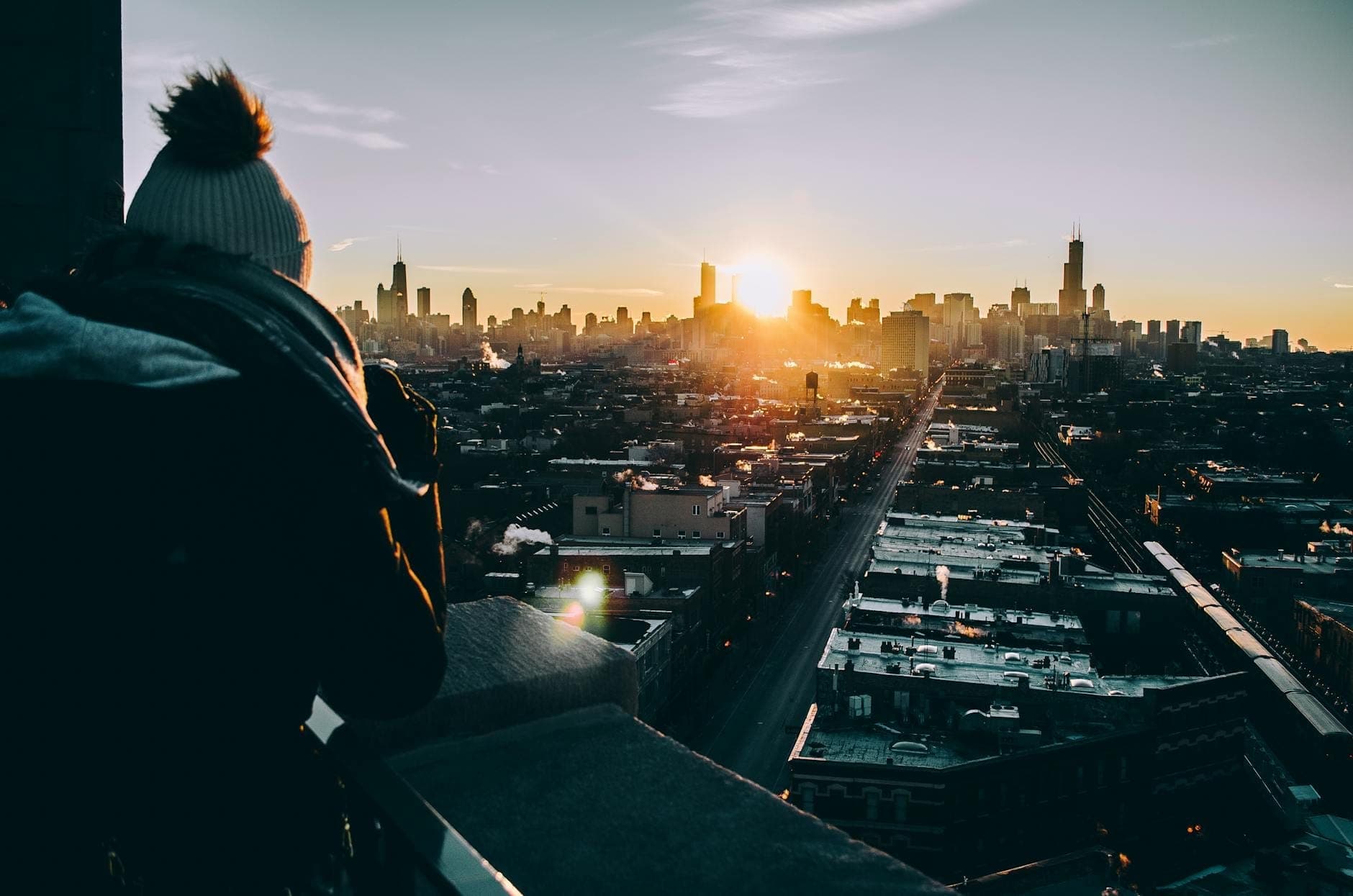 Person standing on a rooftop at sunset enjoying a sweeping view of the Chicago skyline with dramatic light and city buildings visible.